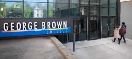 A male and female student walking towards a Casa Loma campus entrance near a George Brown College sign.