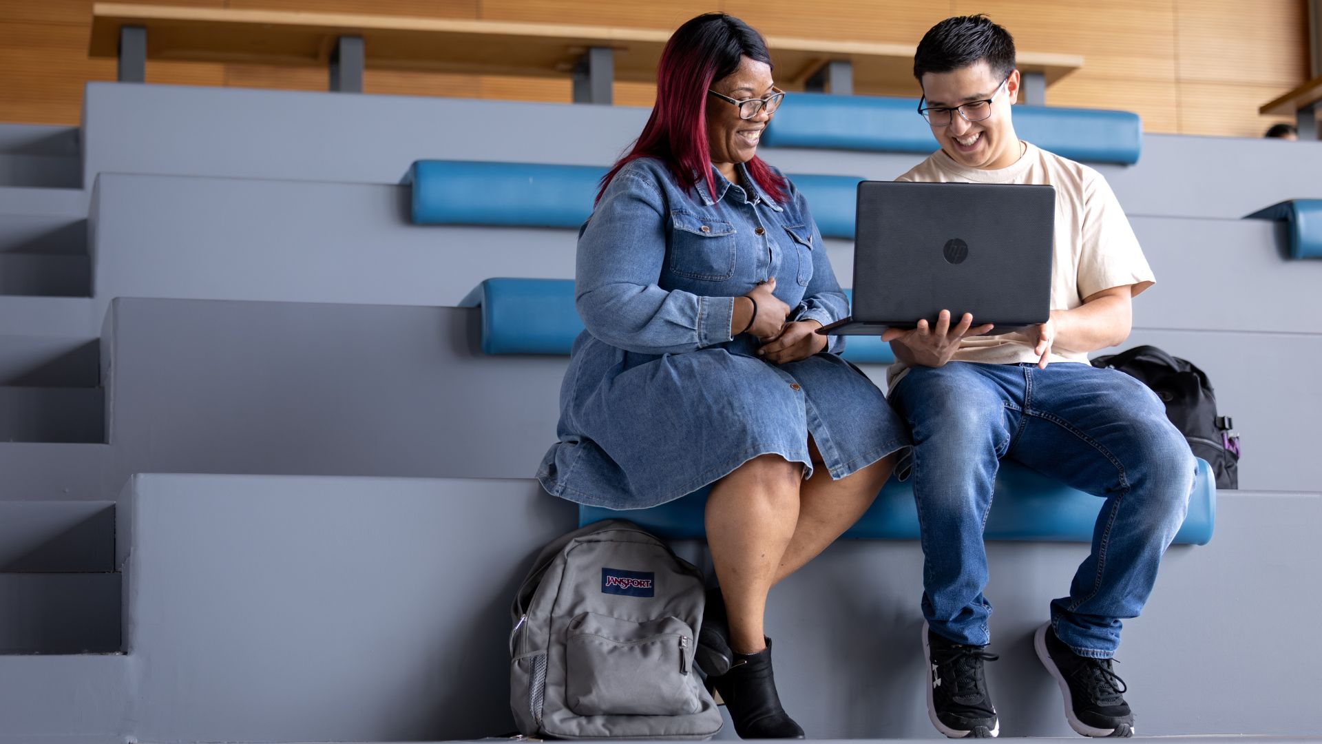 Two students sit next to each other looking at one laptop.