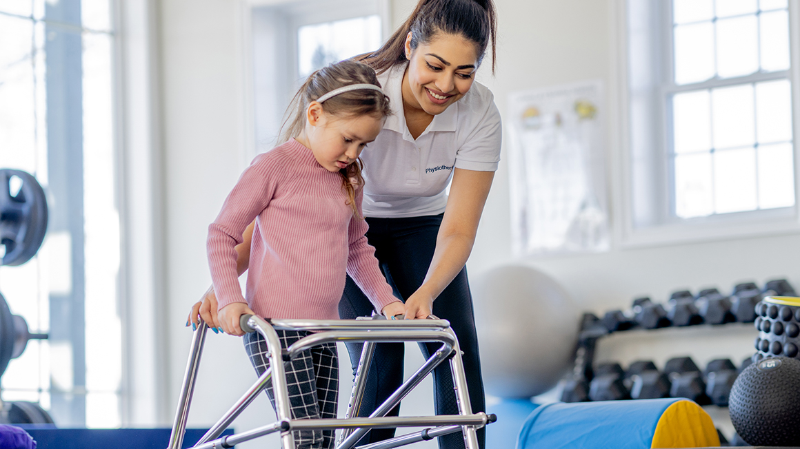 female physical therapy assistant helping a young girl using a walker or mobility assistive device