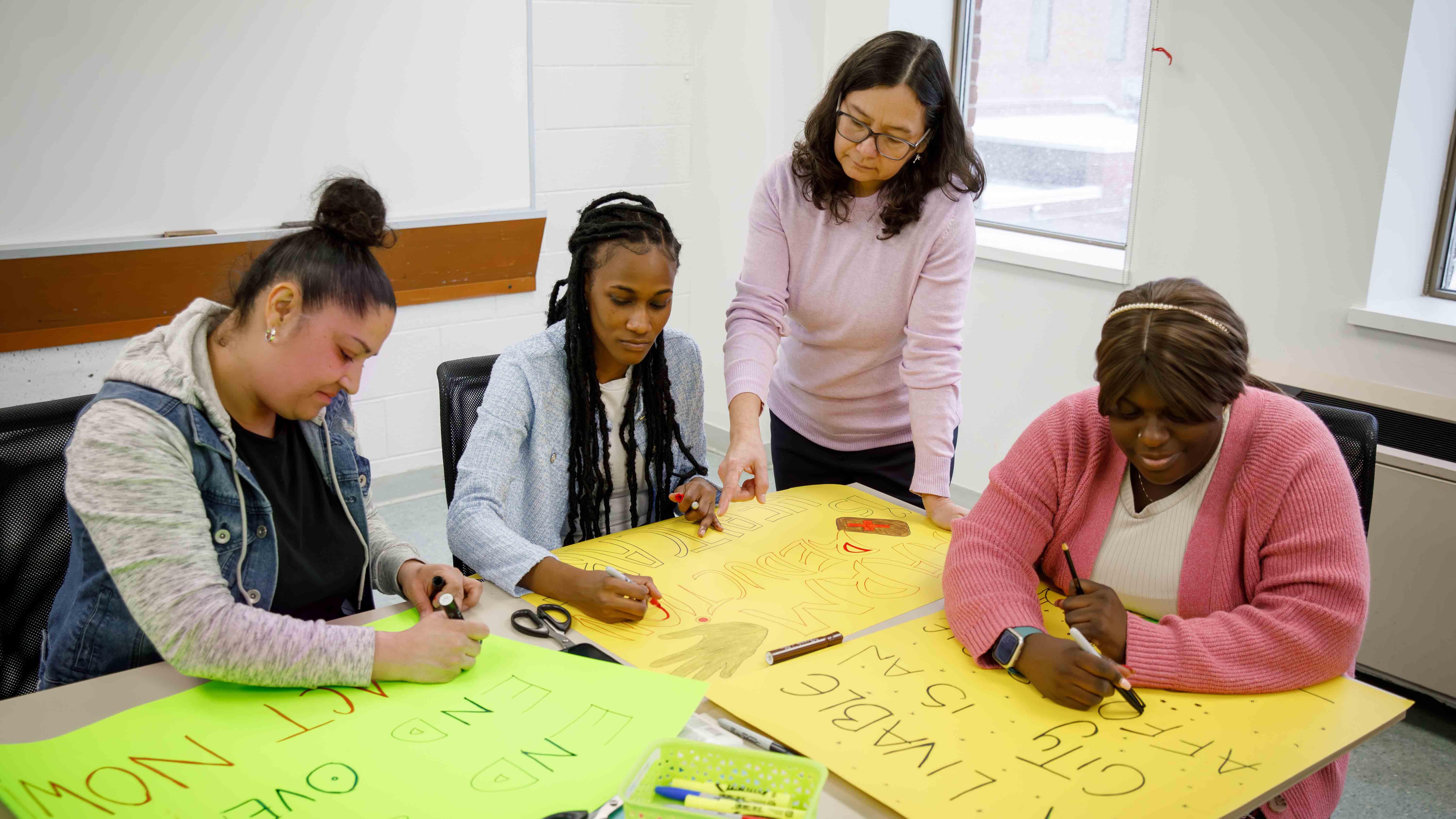 Four people work together at a table, drawing and writing messages on large colourful posters