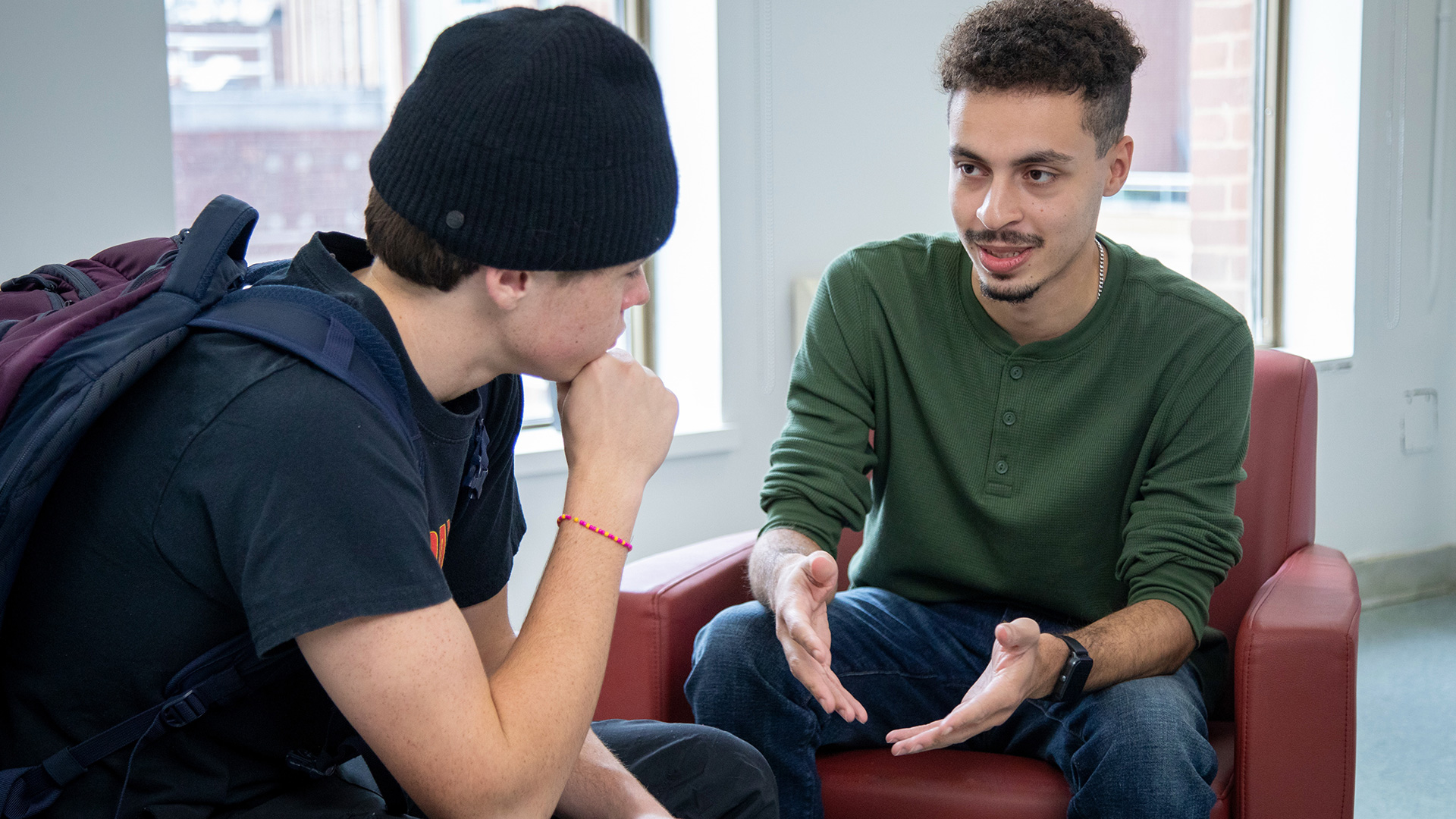 Two students from a child and youth care program sitting together in a bright room, engaged in a supportive one-on-one conversation, with one student actively listening and the other speaking with open hand gestures.