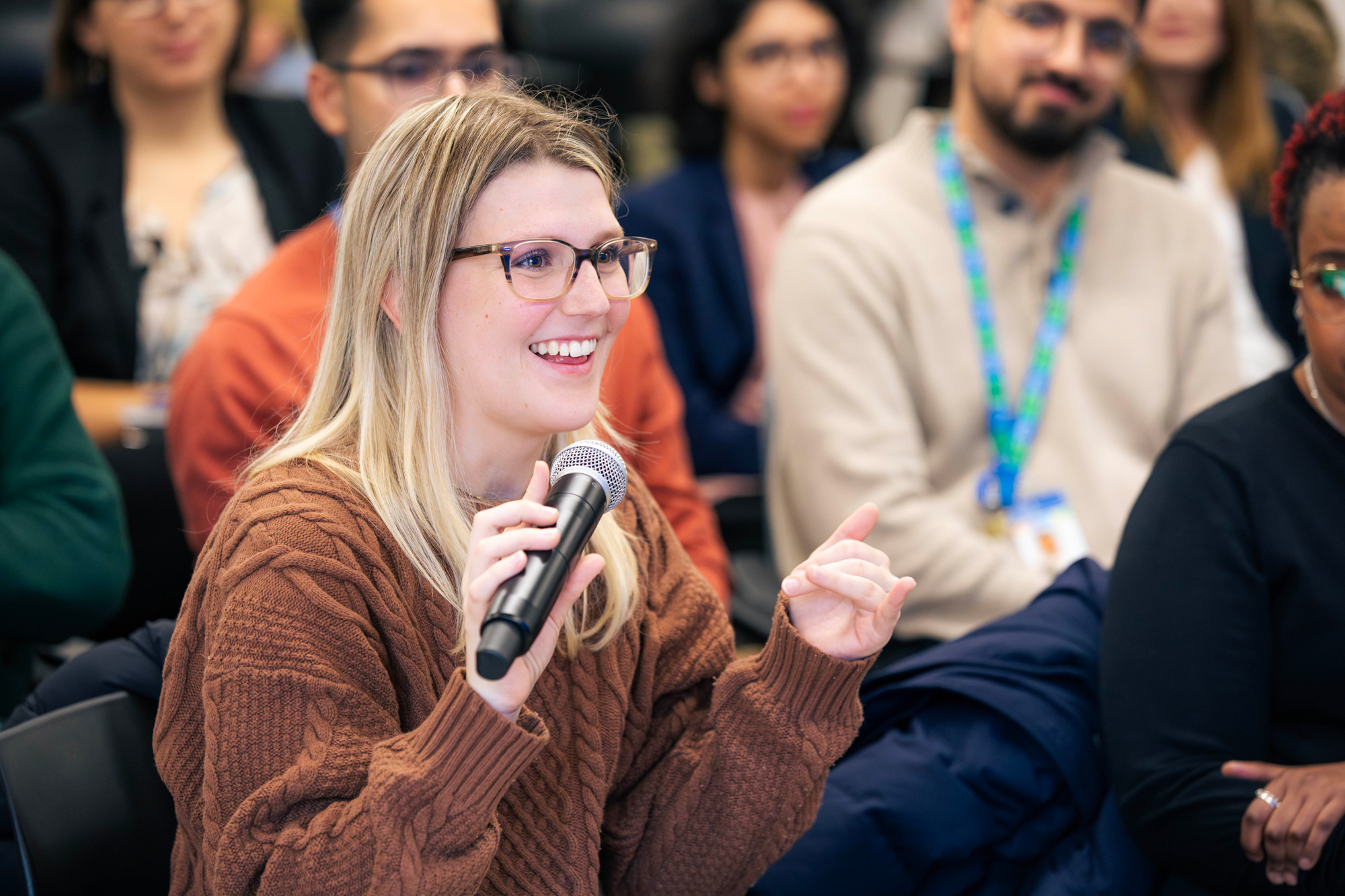 A women in brown top and glasses holds a microphone to ask a question