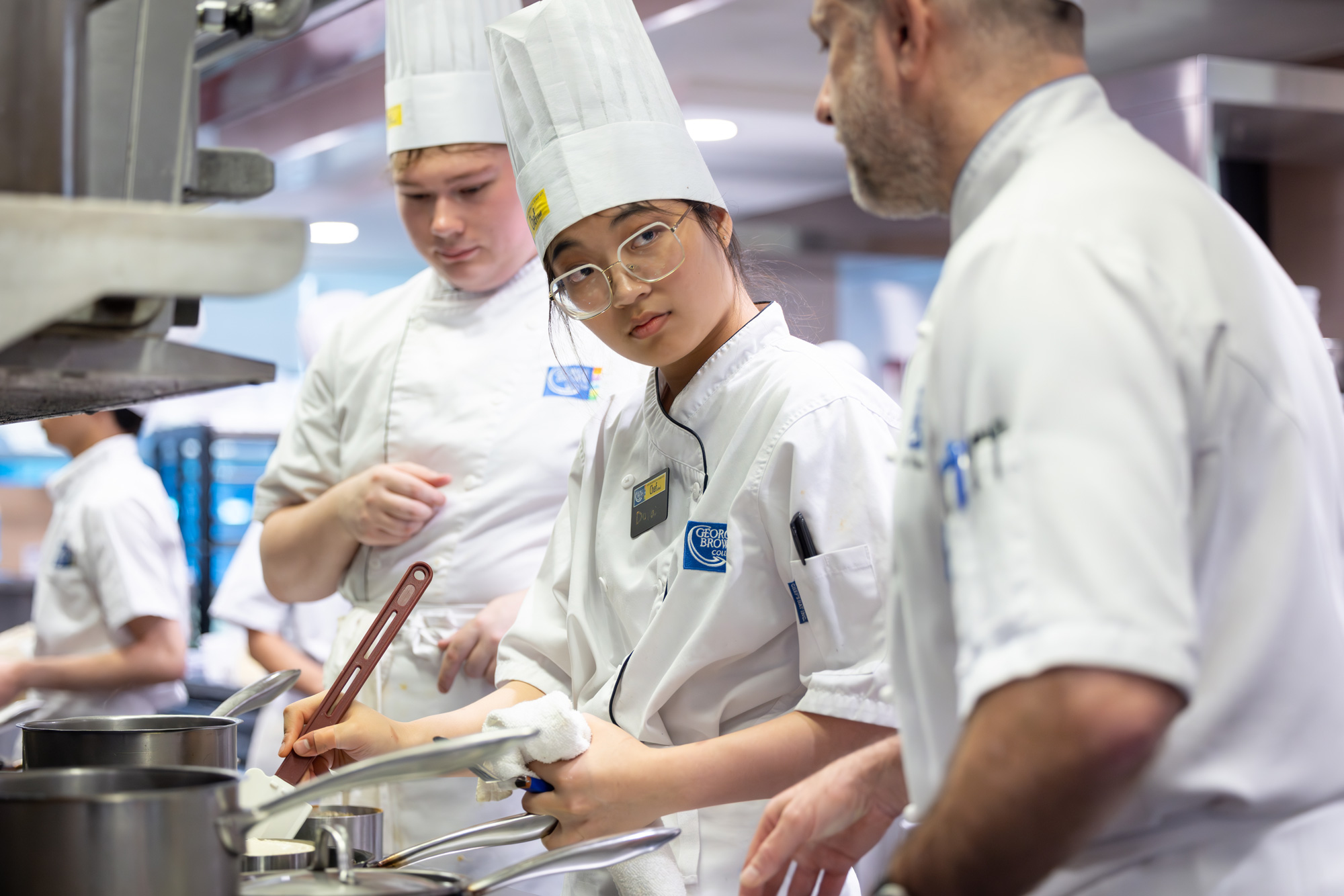 Three chefs in white clothing and chefs' hats stir