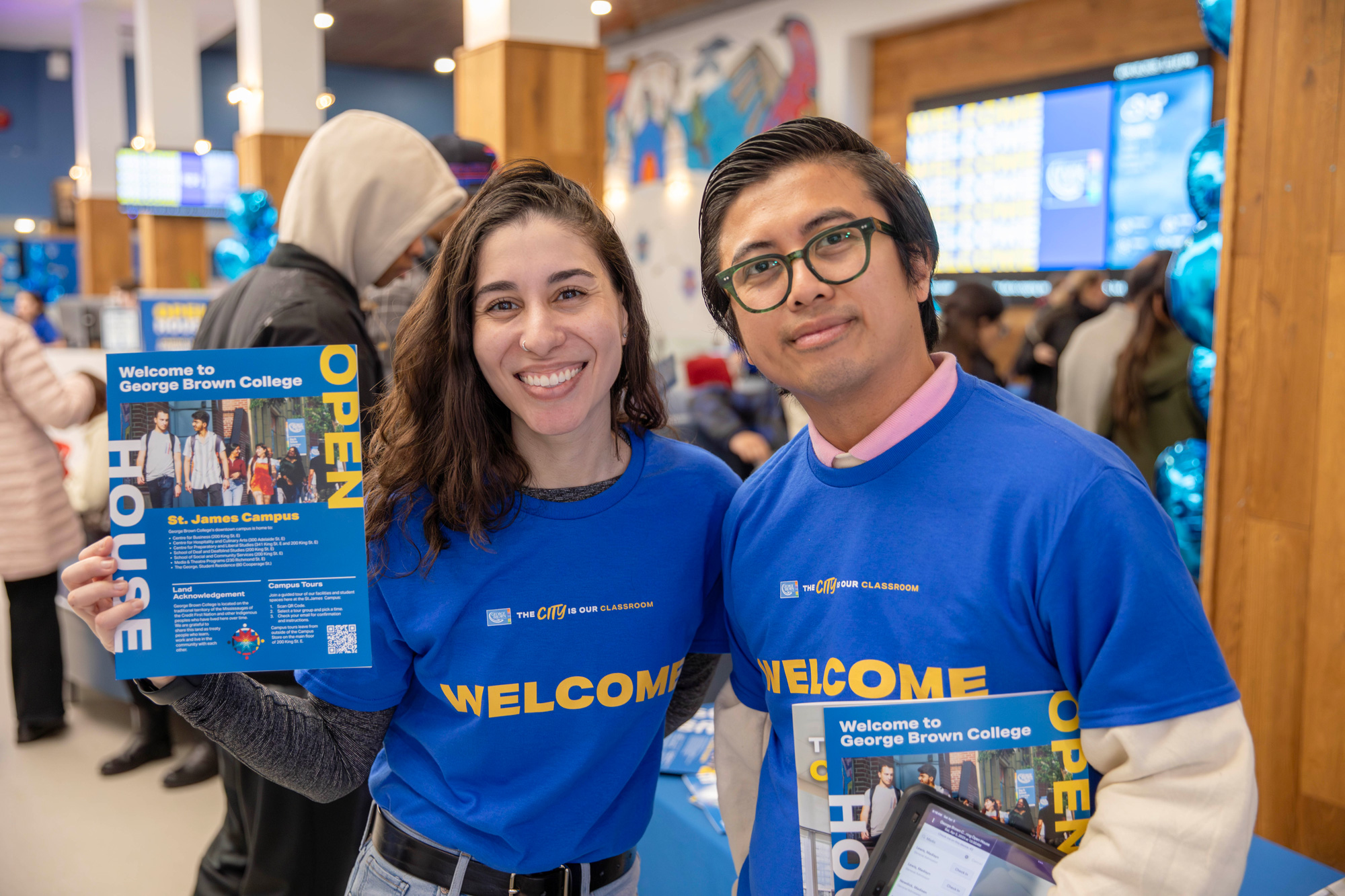 Two students at the open house smile holding campus guides