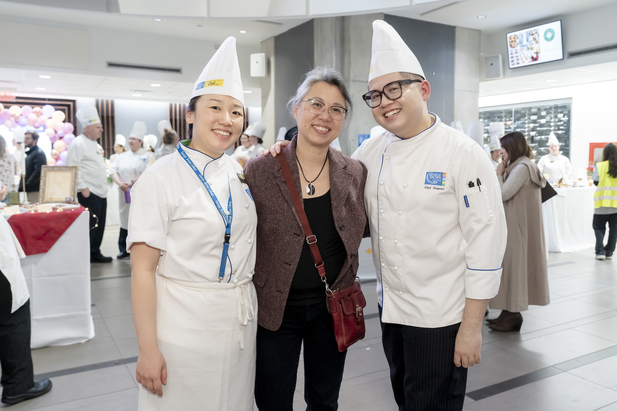 Two students in chef whites stand with a faculty smiling