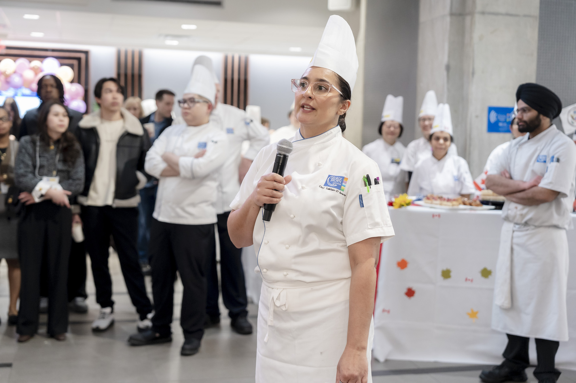 A women in chef whites speaks to a group dressed in chefs whites