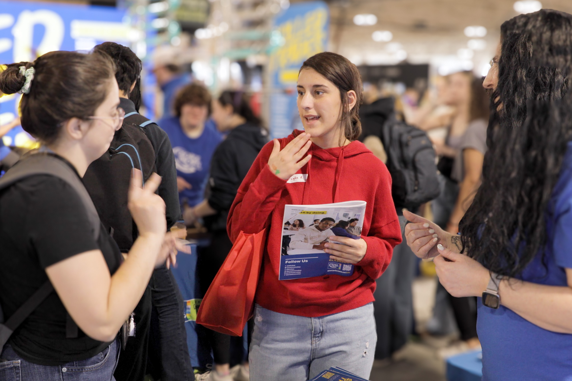 A woman in a read hoodie signs to another