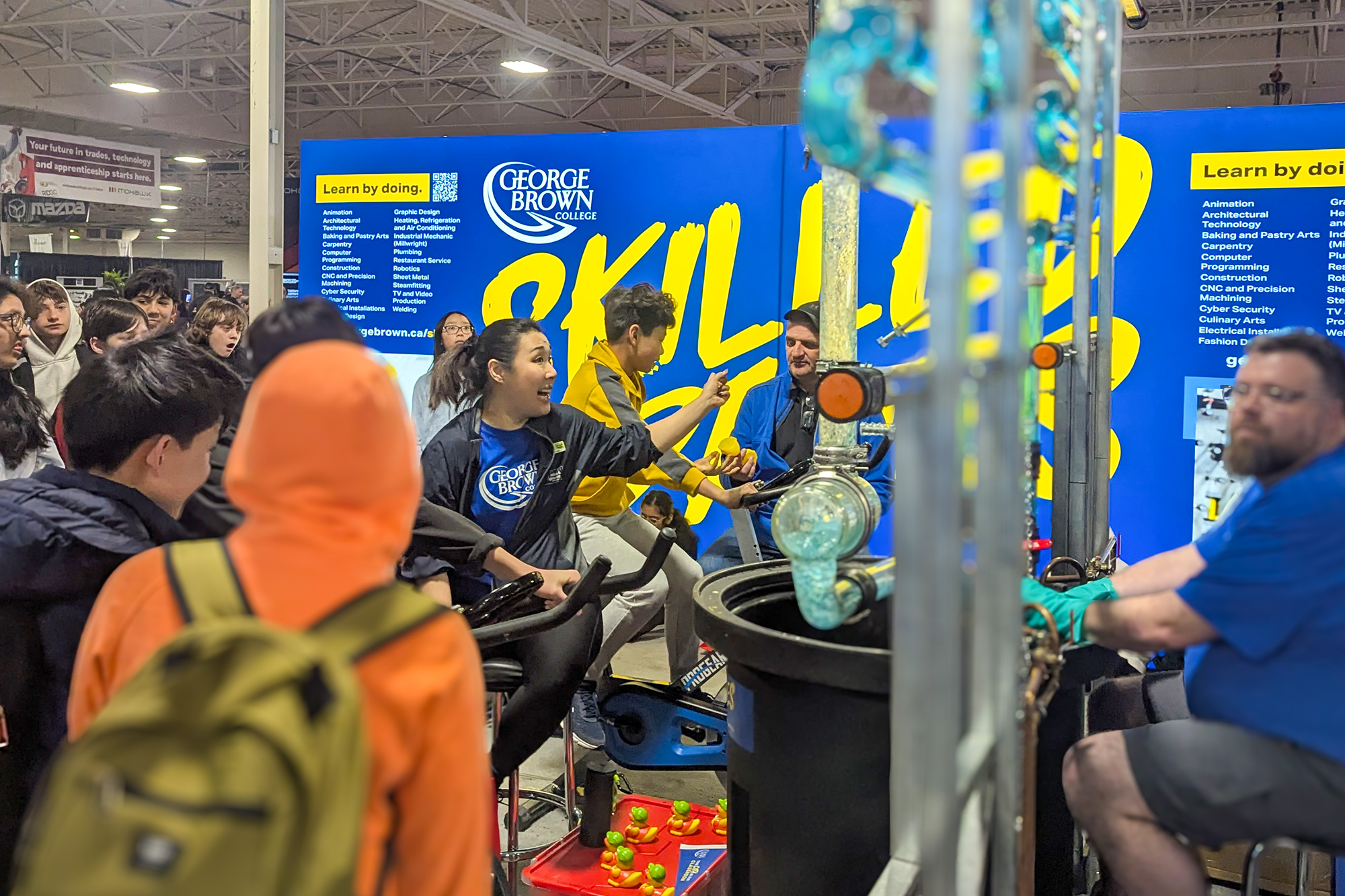 A glass plumbing display with blue liquid surrounded by onlookers