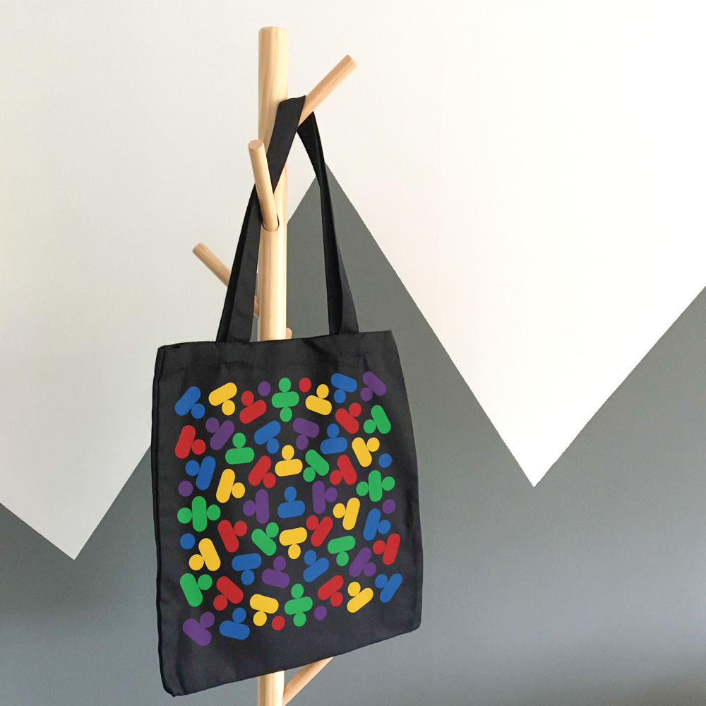 A black tote with a colourful imprint hangs on a wooden coat rack