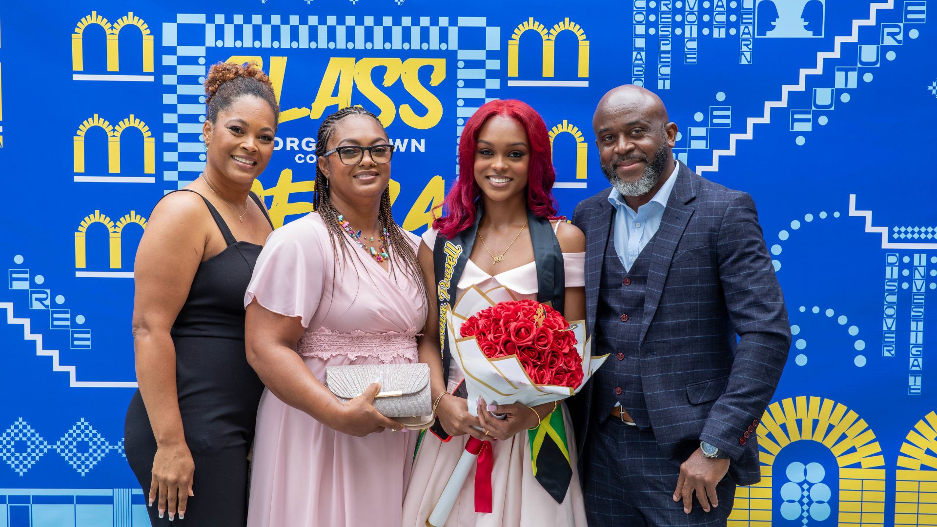 four people standing in formal sear in front of a GBC banner, looking like a family celebrating a graduate