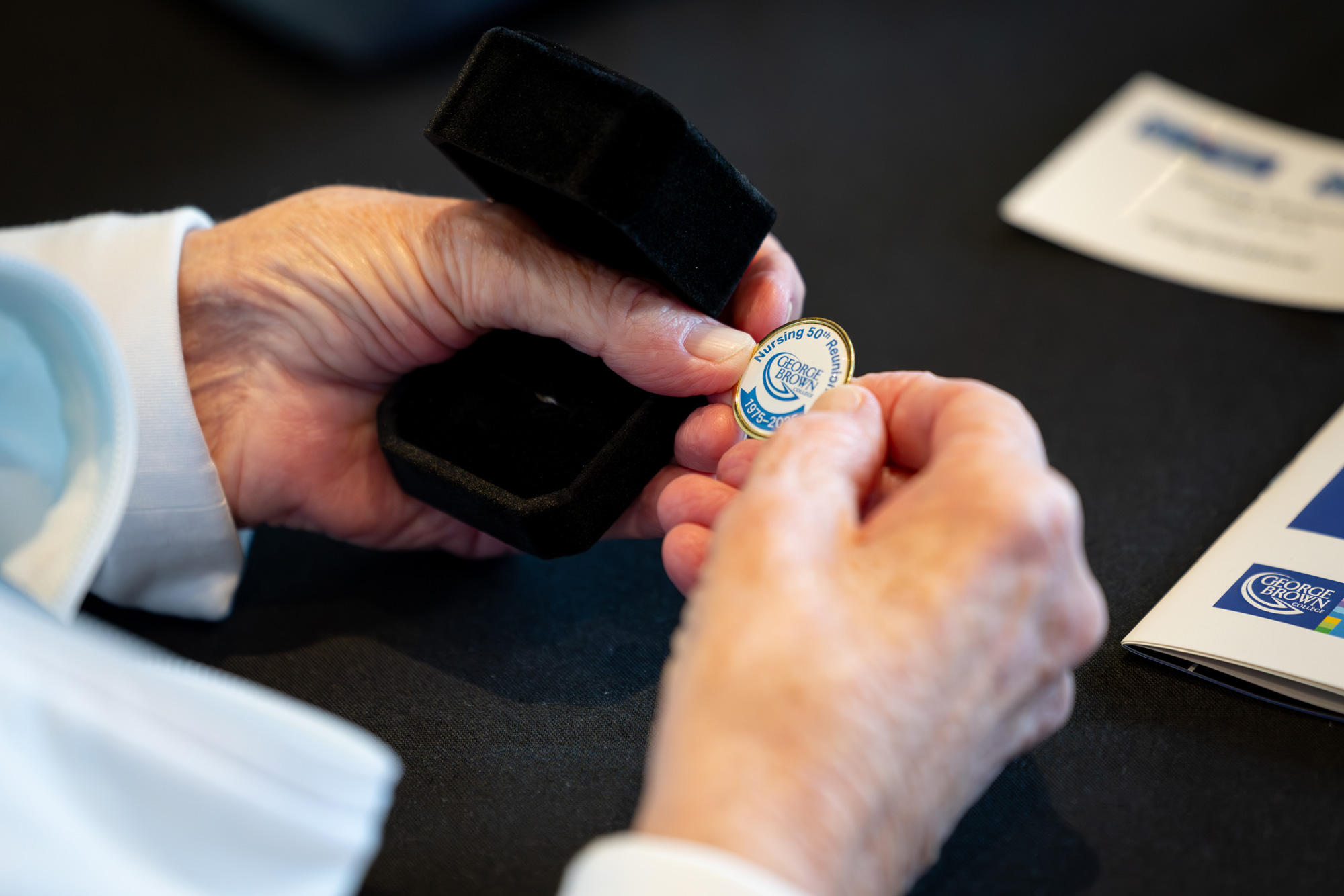 A person holds the 50th reunion commemorative nursing pin with a black background