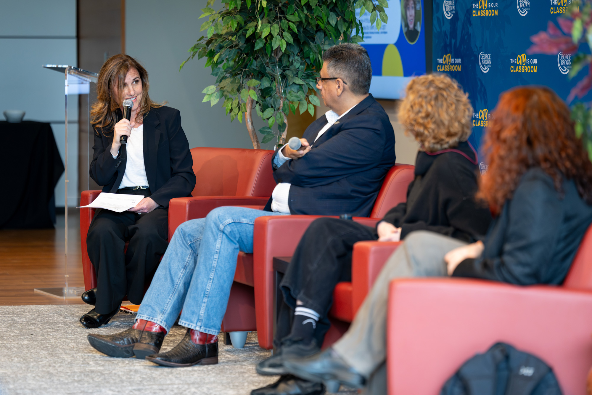 A seated women with microphone speaks to a group of Pen Writer panelists