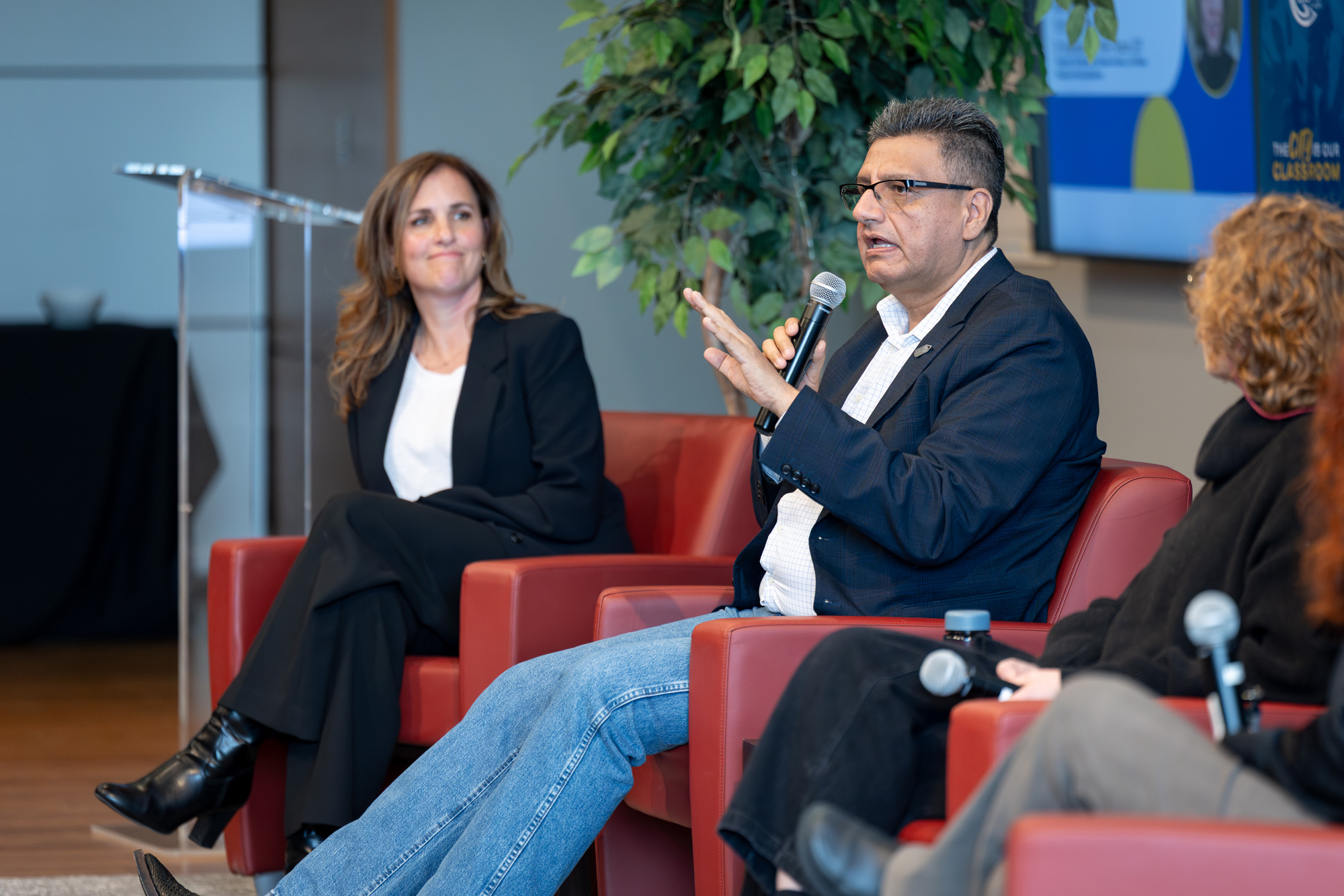 A seated man with microphone speaks to the audience at the Pen Writer panelists