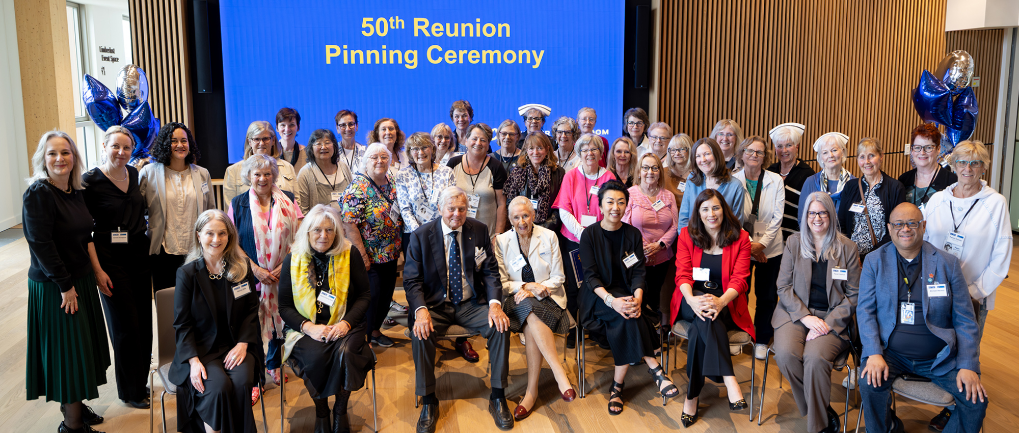 Nursing alumni and George Brown College leadership pose in front of a screen with the text 50th Reunion Pinning Ceremony