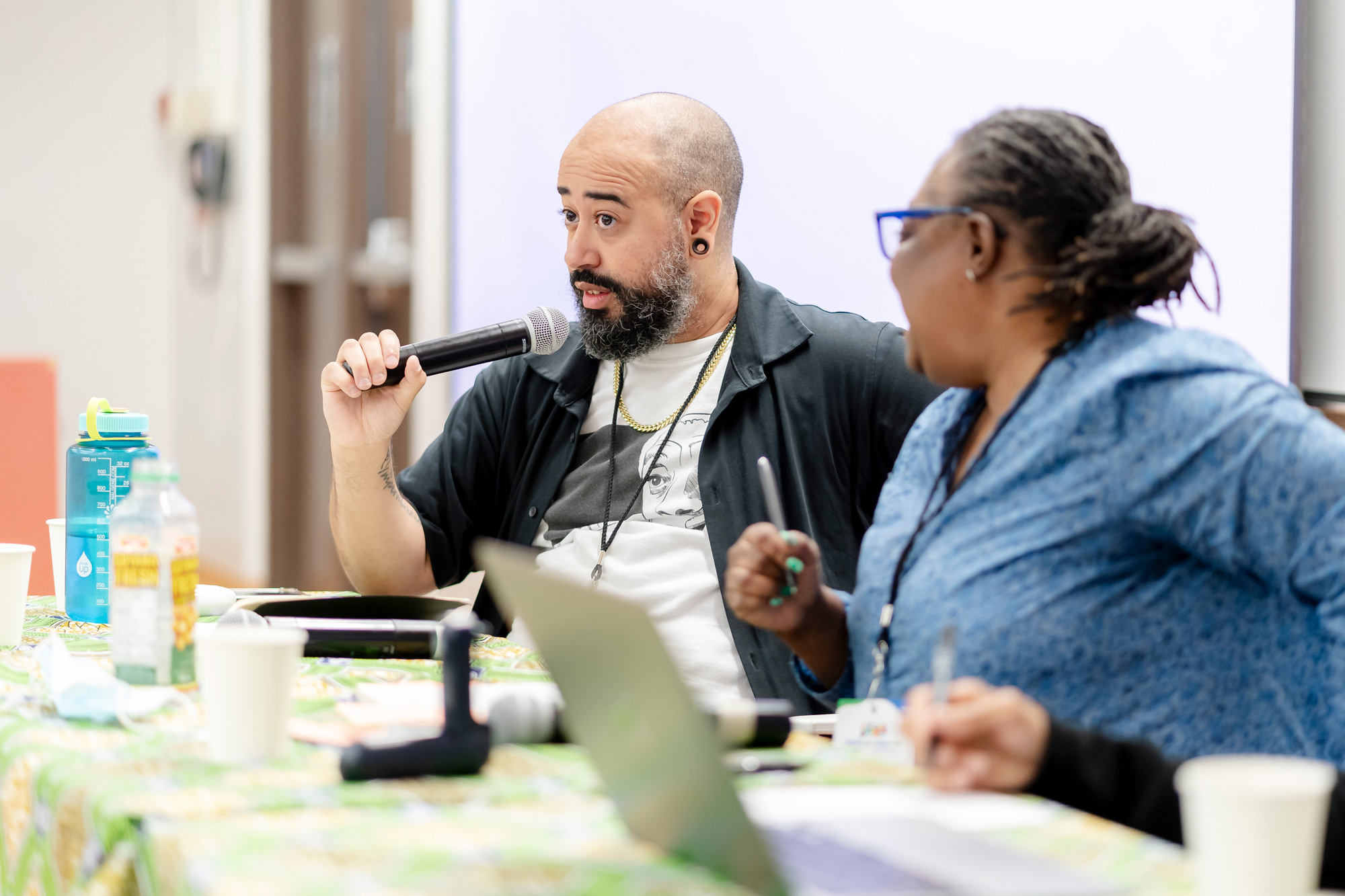 A man holds up a microphone and speaks as a panelist at the Black Chat and Chill event