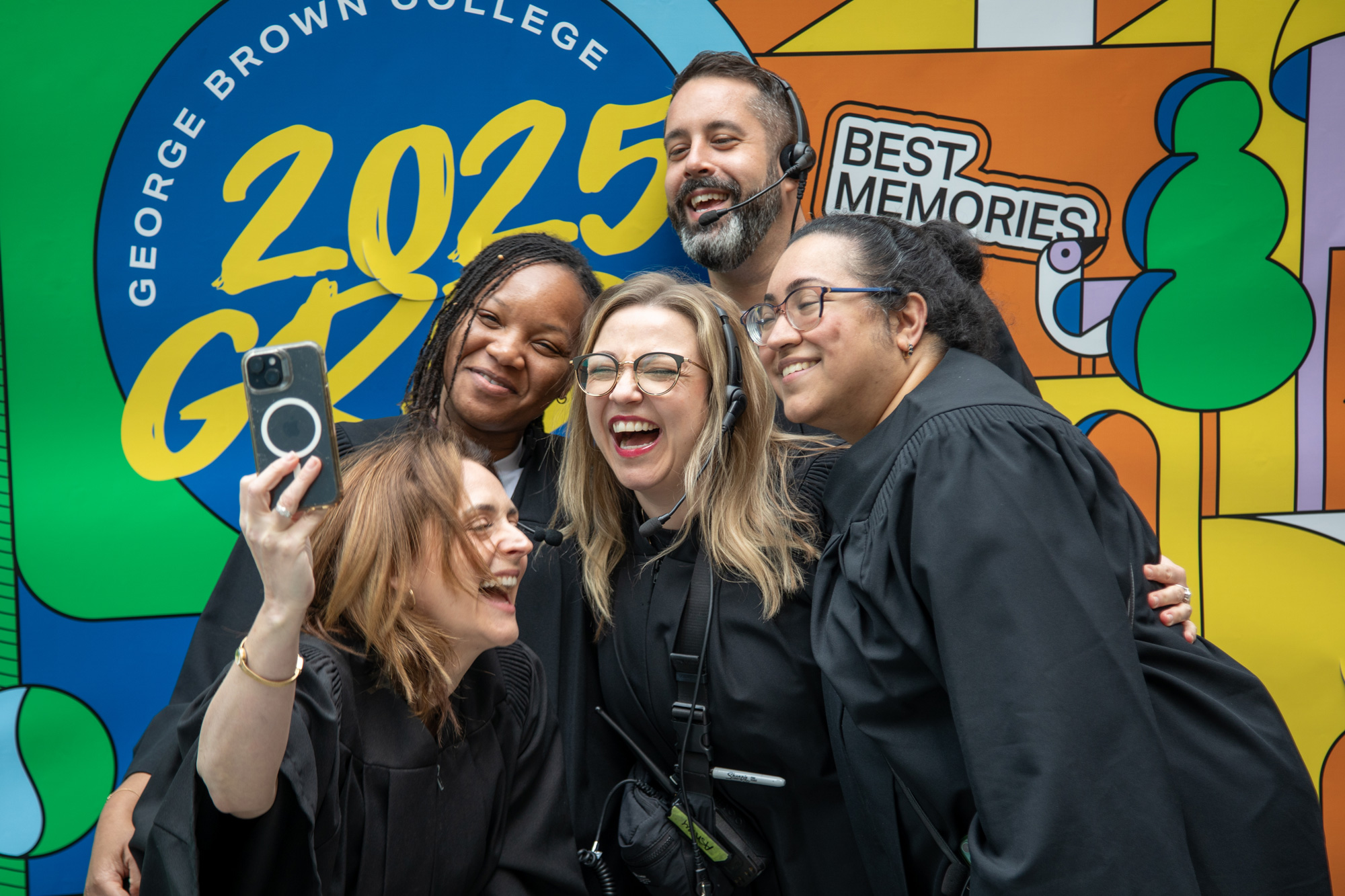 Convocation staff celebrate with a selfie in front of a bright mural