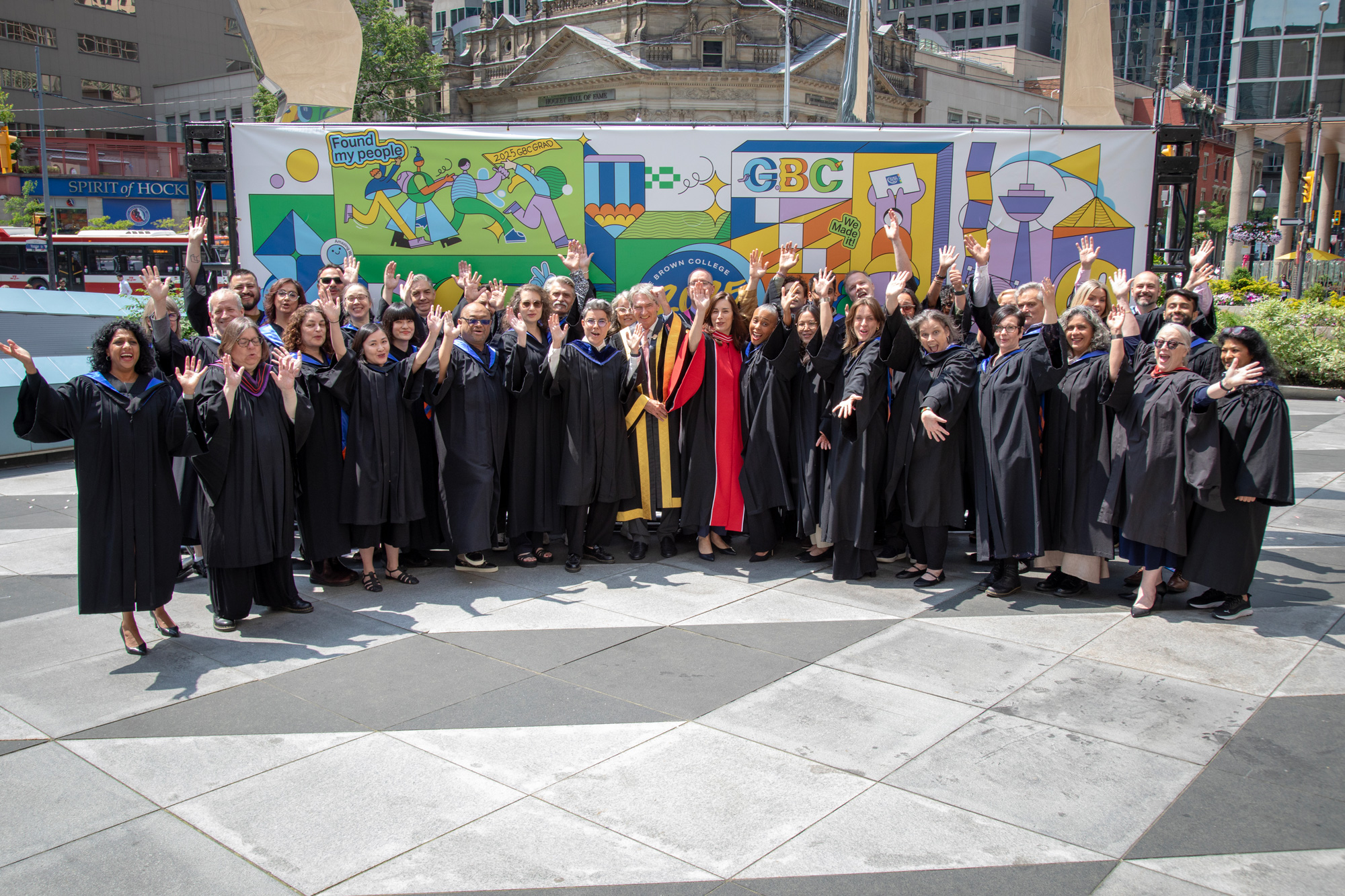 A group of faculty and leadership pose in front of a brightly coloured mural at the 2025 convocation ceremonies