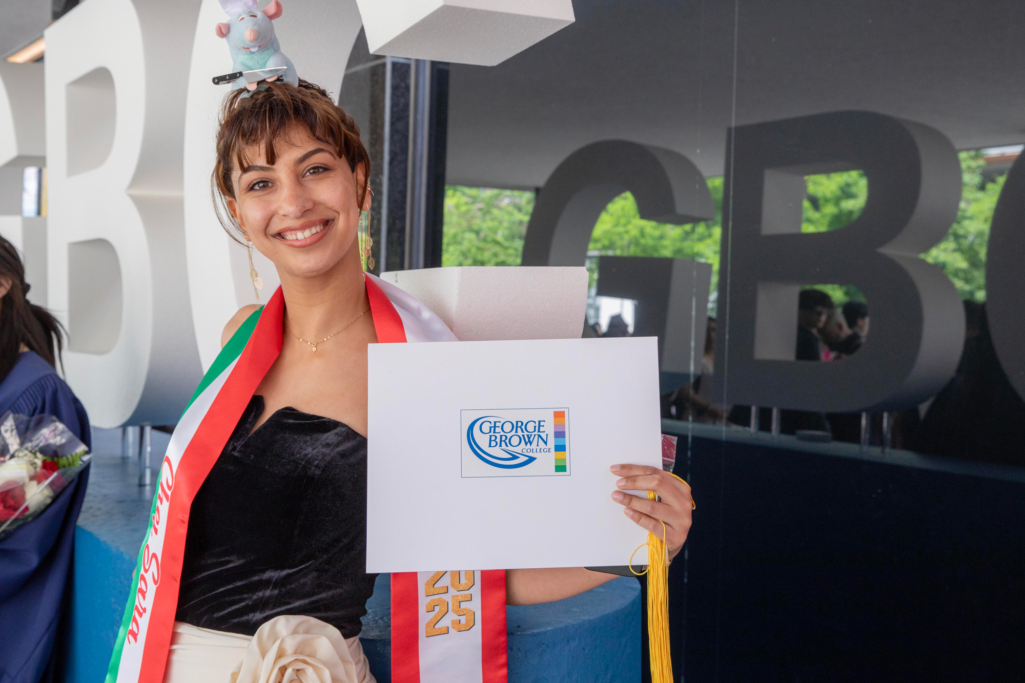 A graduating student holds up their credential in front of a GBC sign