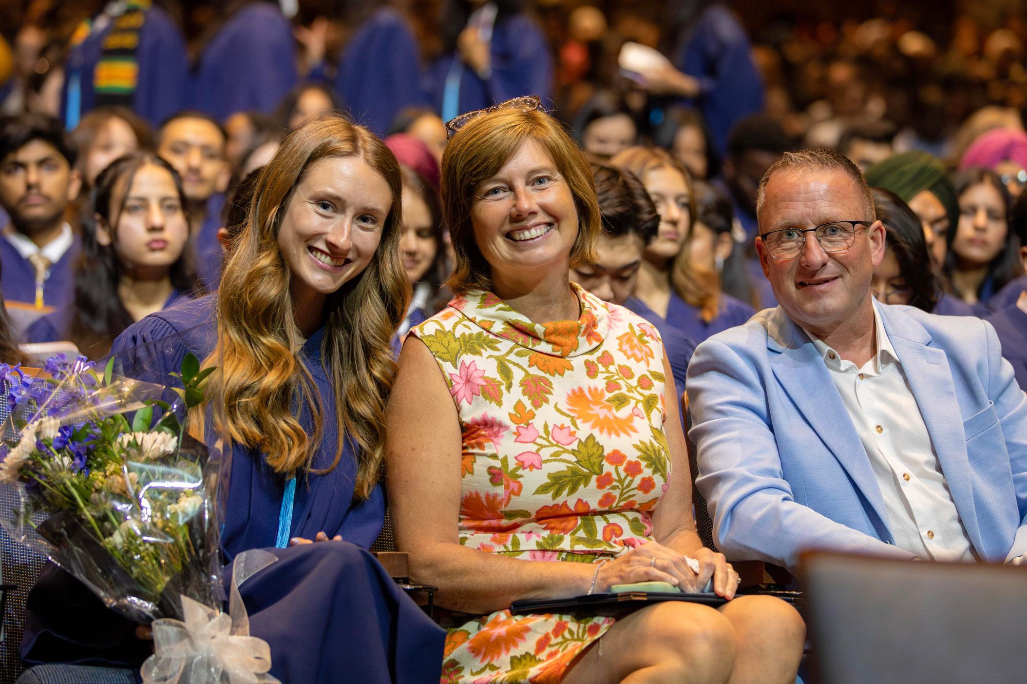 A graduating student is seated with their family holding flowers and their credential