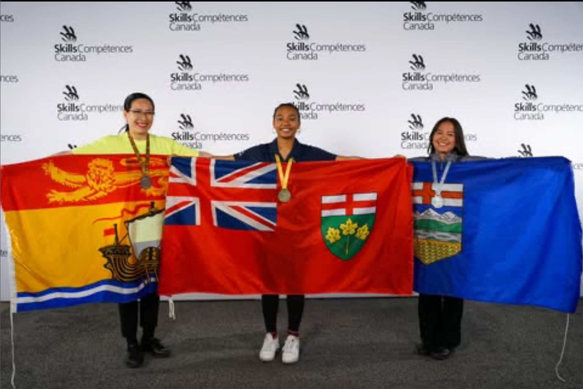 Three medal winners at the Skills Canada competition hold up flags from their provinces