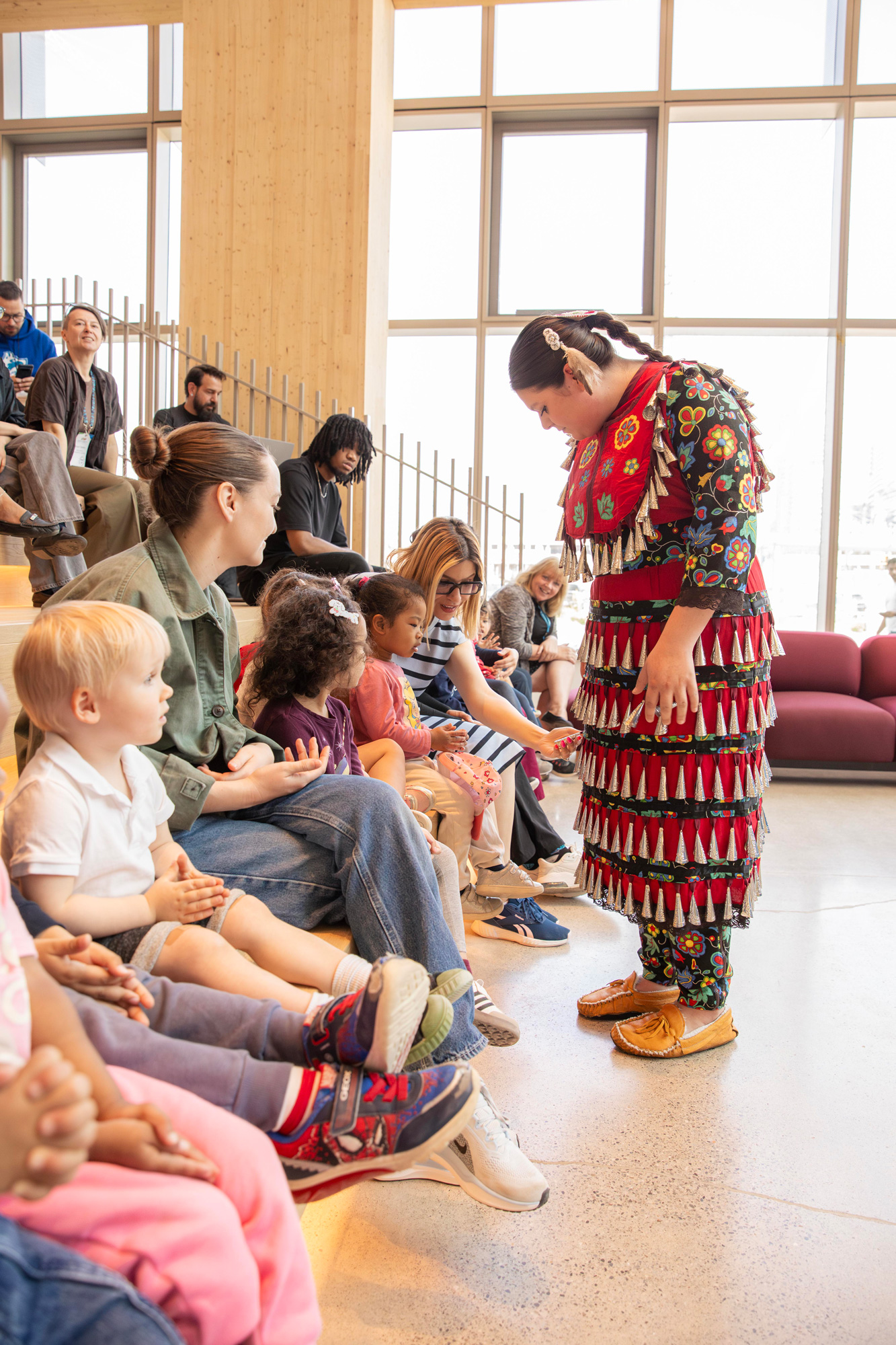A jingle dancer shows her outfit to the child care children
