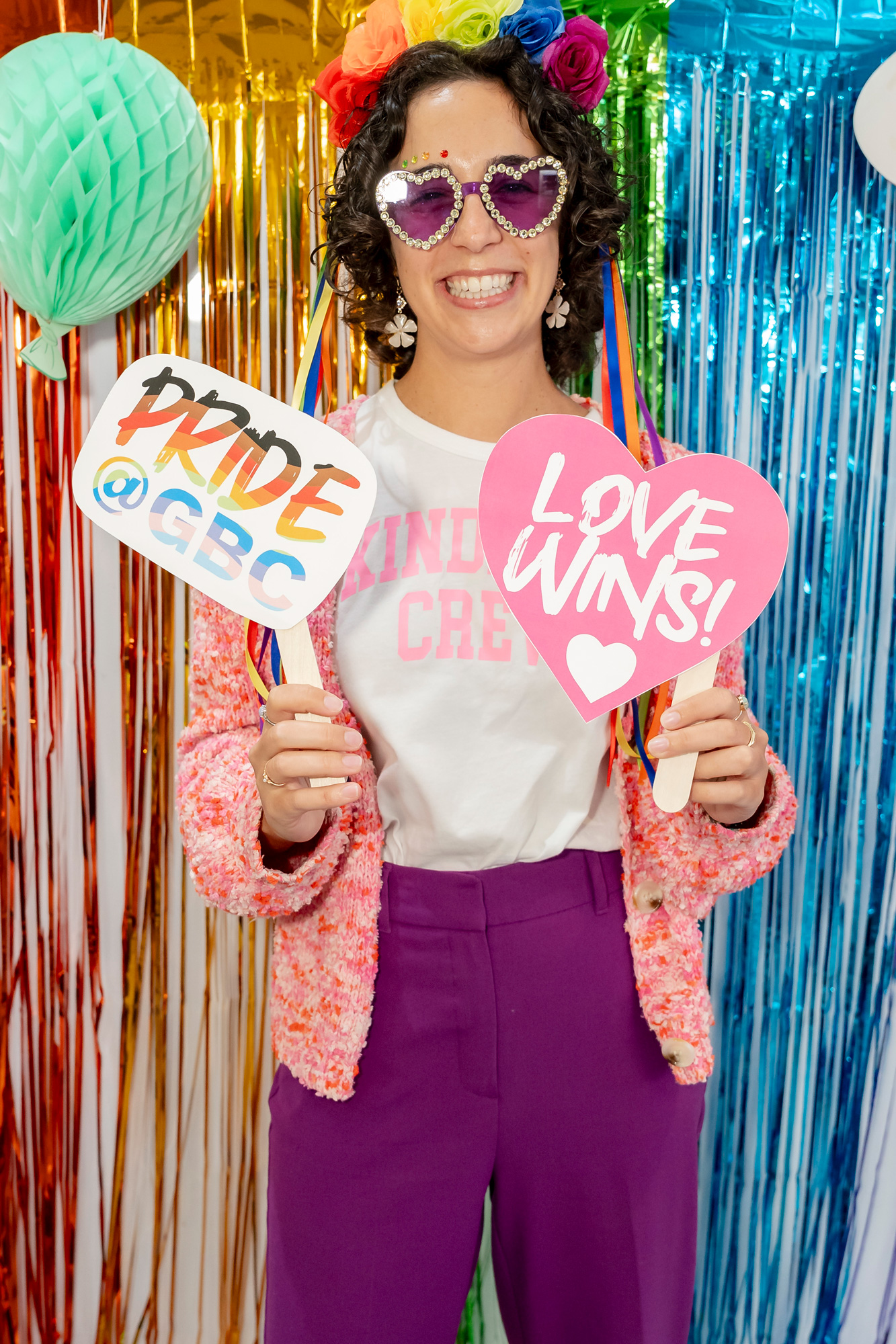 A woman with heart shaped glasses holds up signs, Pride at GBC, and love wins