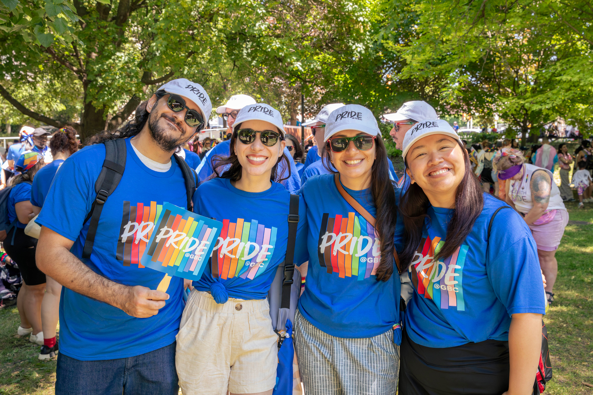 A group poses in bright blue Pride at GBC t-shirts holding fans in an outdoor space