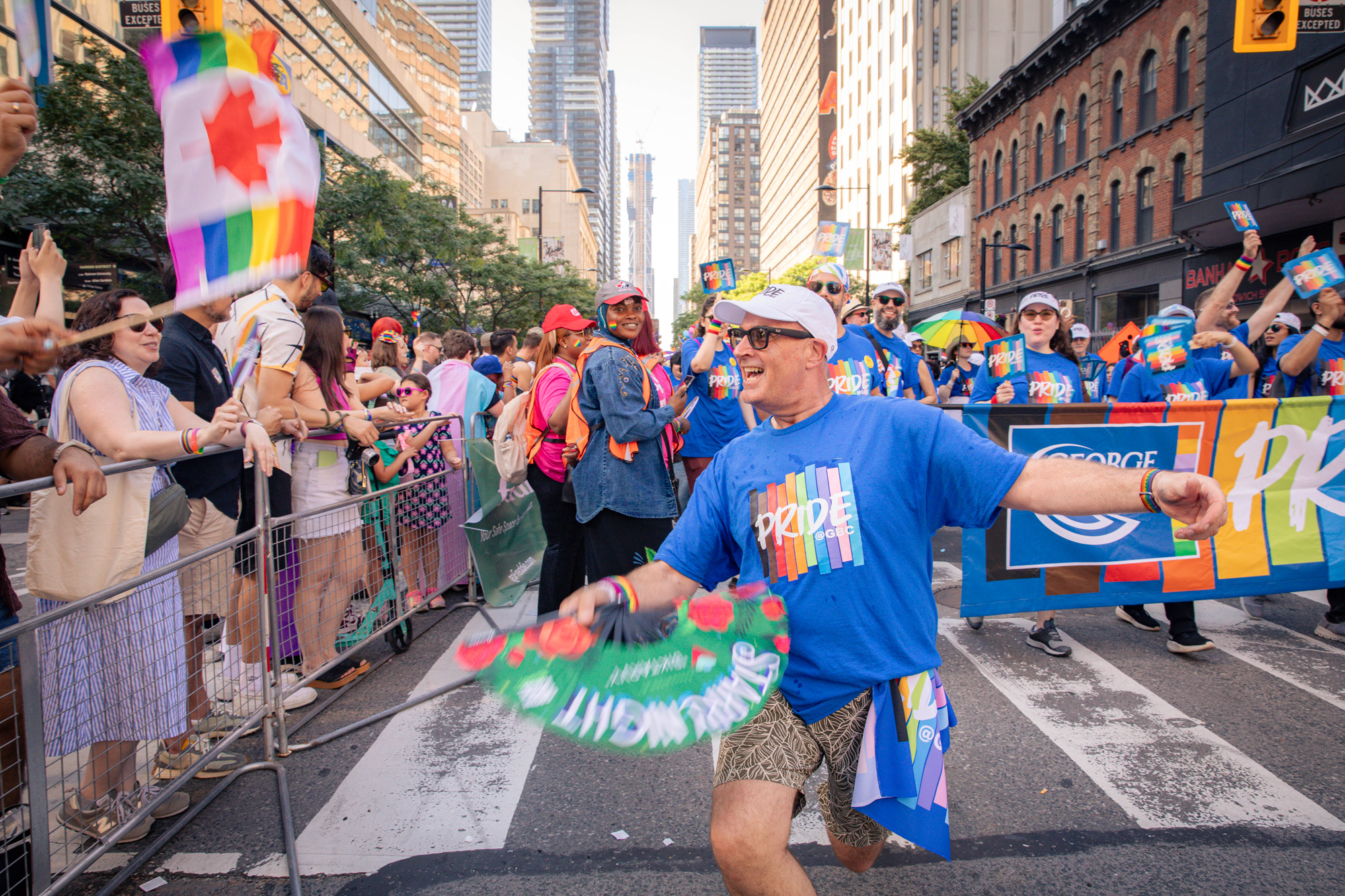 A GBC staff in bright blue Pride at GBC t-shirt waves a green fan in the Pride parade