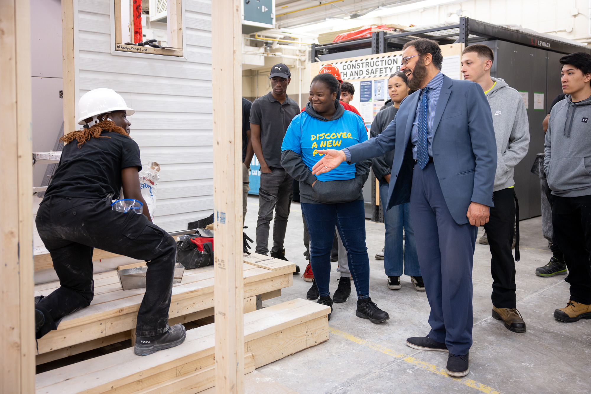 A student works on the exterior of a building while a group stops on a tour to watch