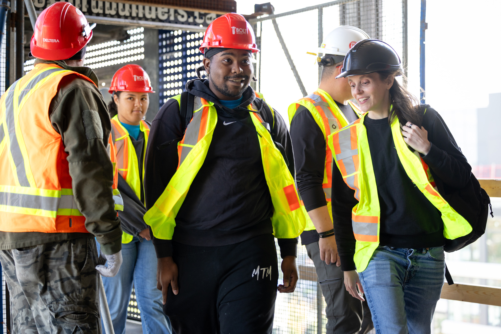A group of students in high vis vests and red hard hats tour a building site