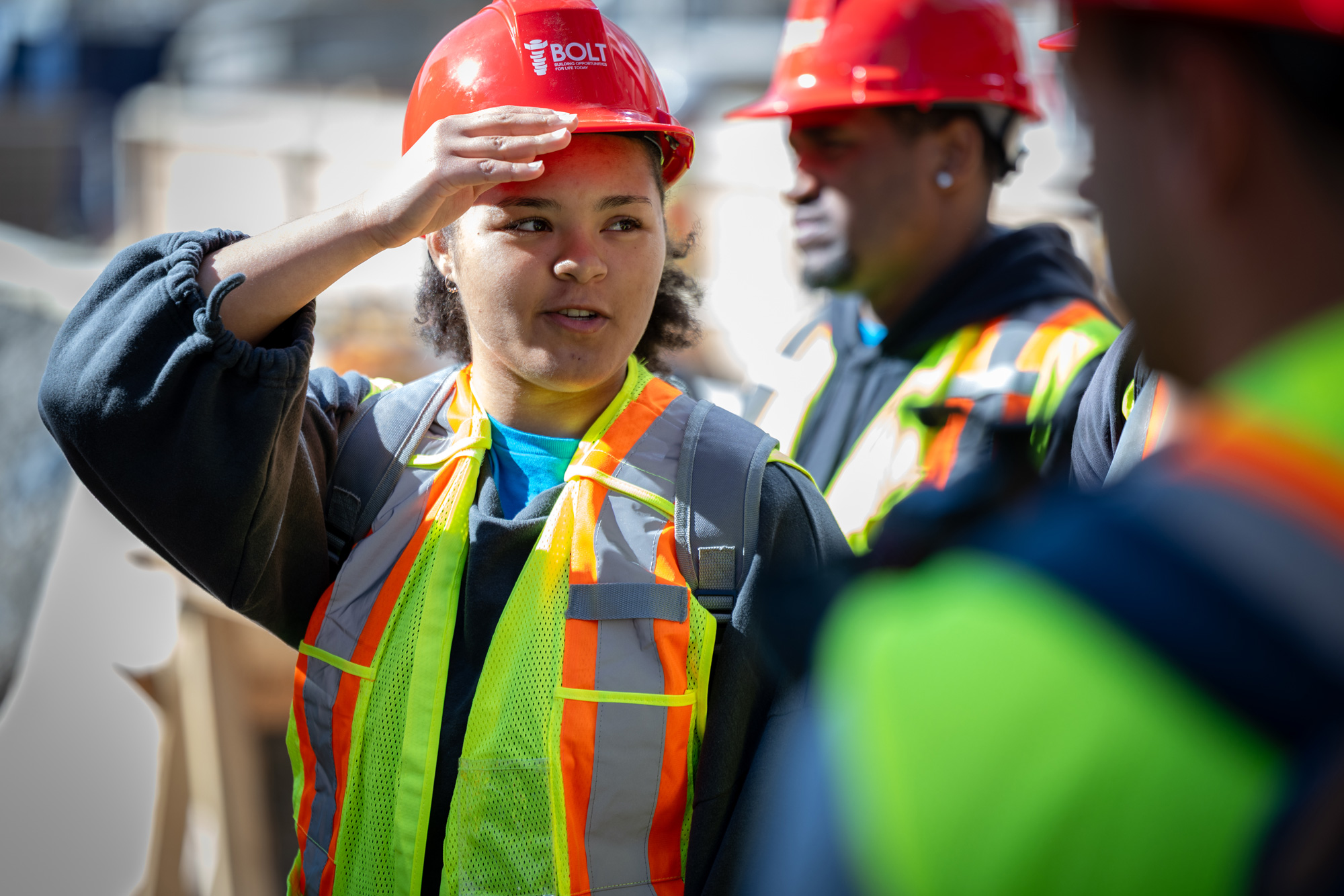 A student in a high vis vest and red hardhat chats with peers on a site tour