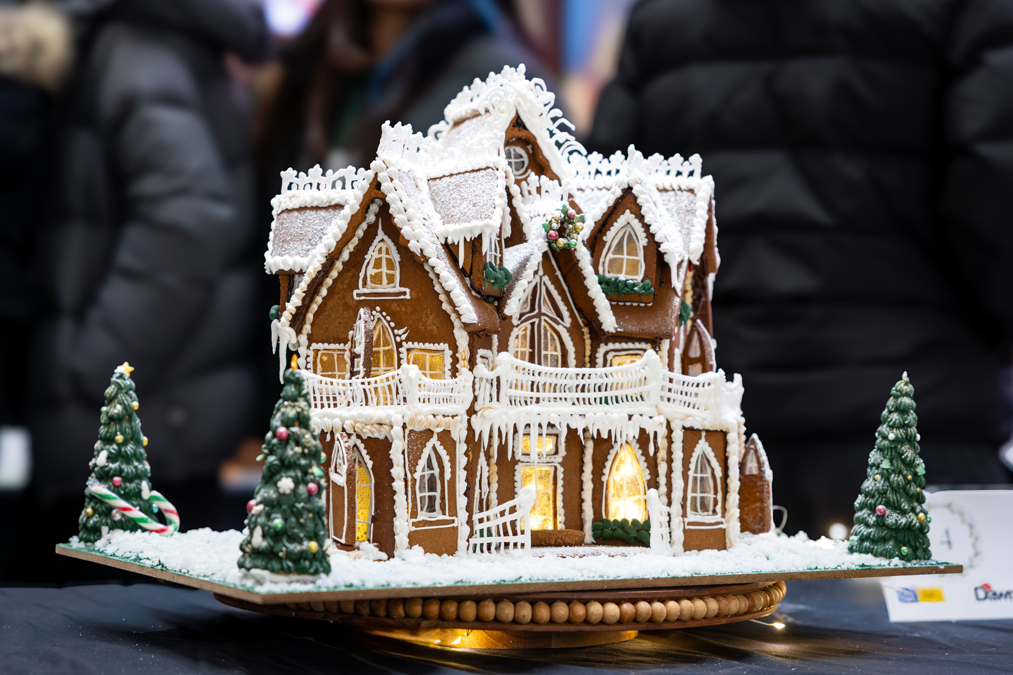 A victorian inspired gingerbread house with intricate windows, railings, and peaked roofs, surrounded by snow