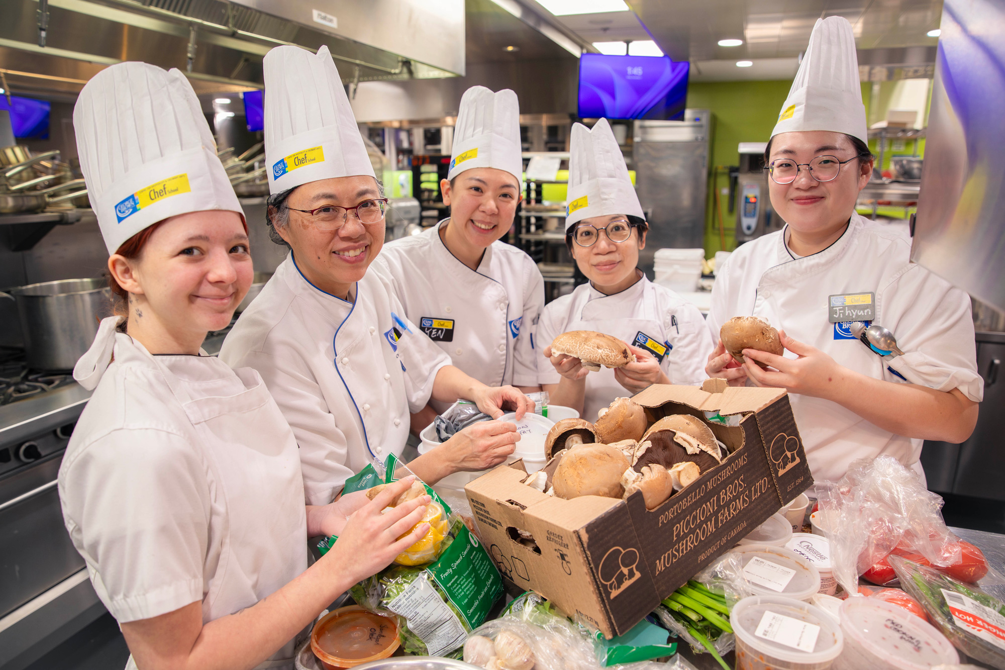Student chefs surround a table of ingredients in the Chef School kitchens