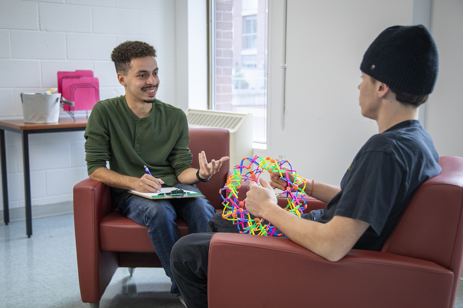 Two people having a conversation. One is taking notes and the second one is playing with a jumbo expand-a-ball
