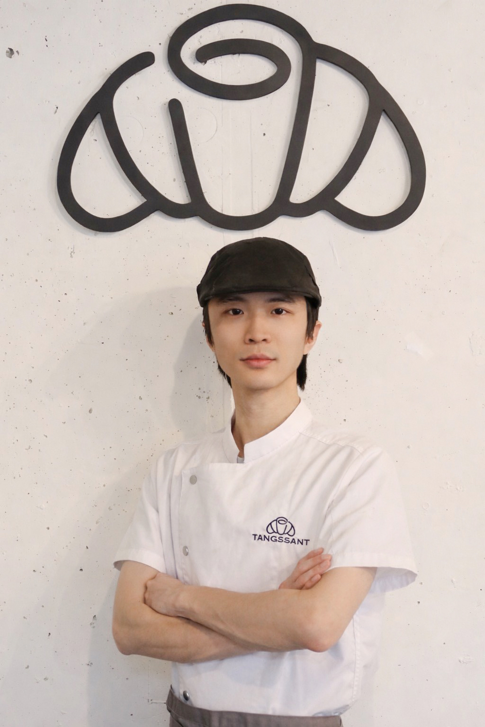 Zhaofeng Huang stands in his cafe with a croissant sign behind him