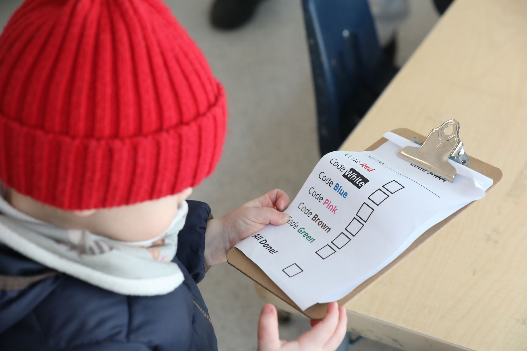 A toddler in a red hat looks at a clipboard with code alerts
