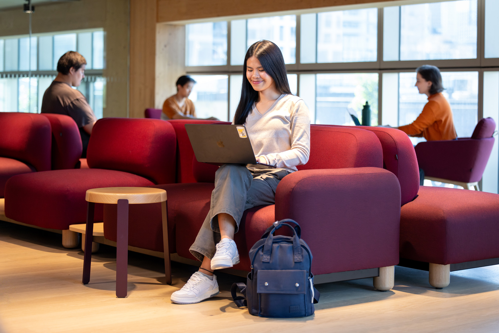 A student seated on a red chair using a laptop in Limberlost Place