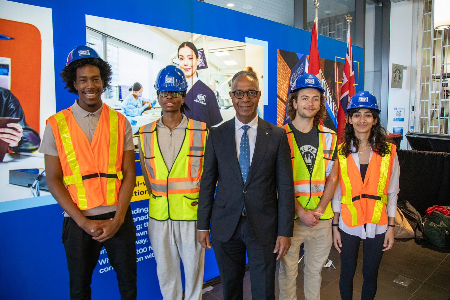 President Fearon takes a photo with George Brown students in hard hats and high-vis vests.