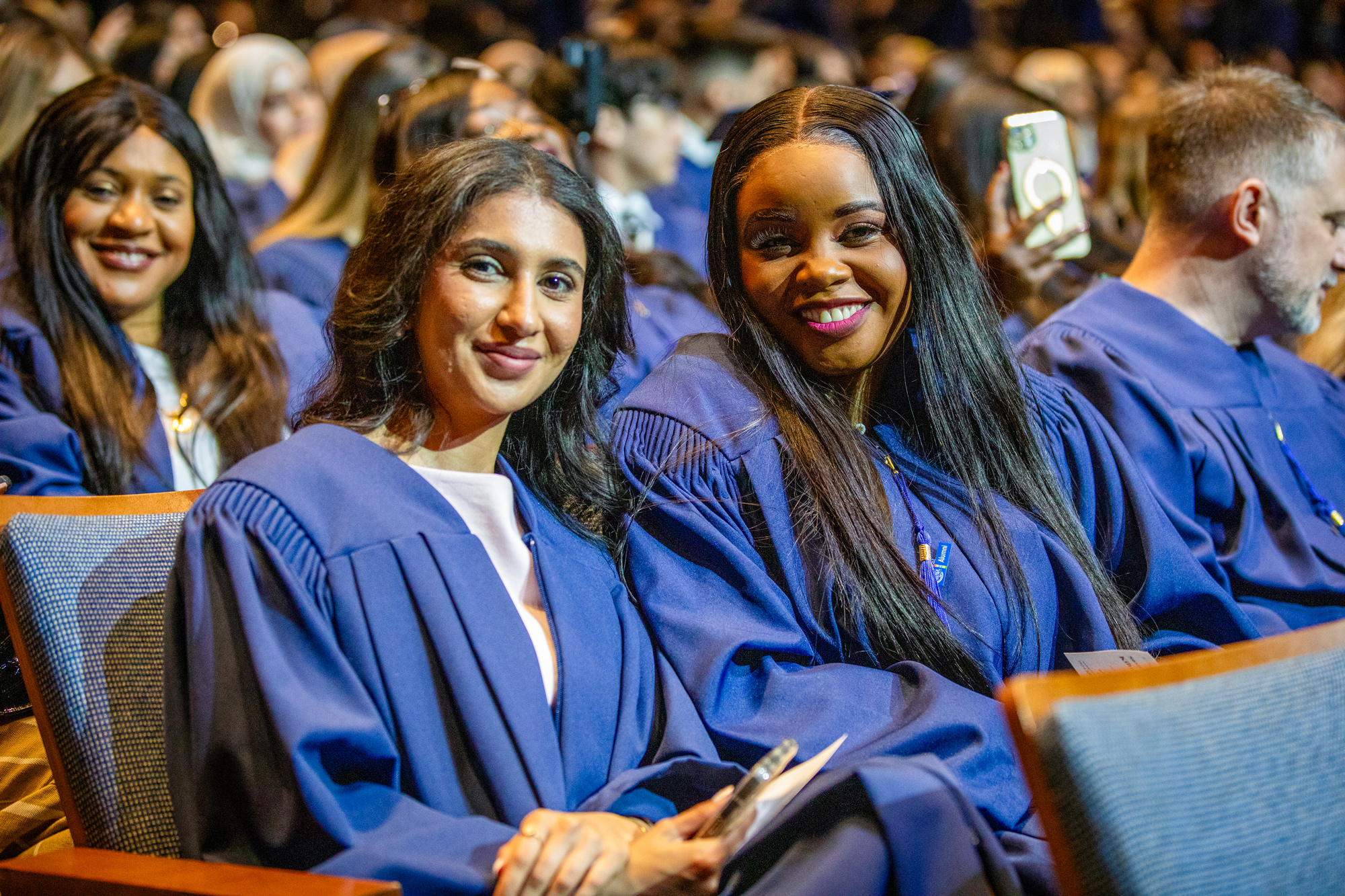 George Brown grads seated in Meridian Hall smile for the camera surrounded by their classmates.