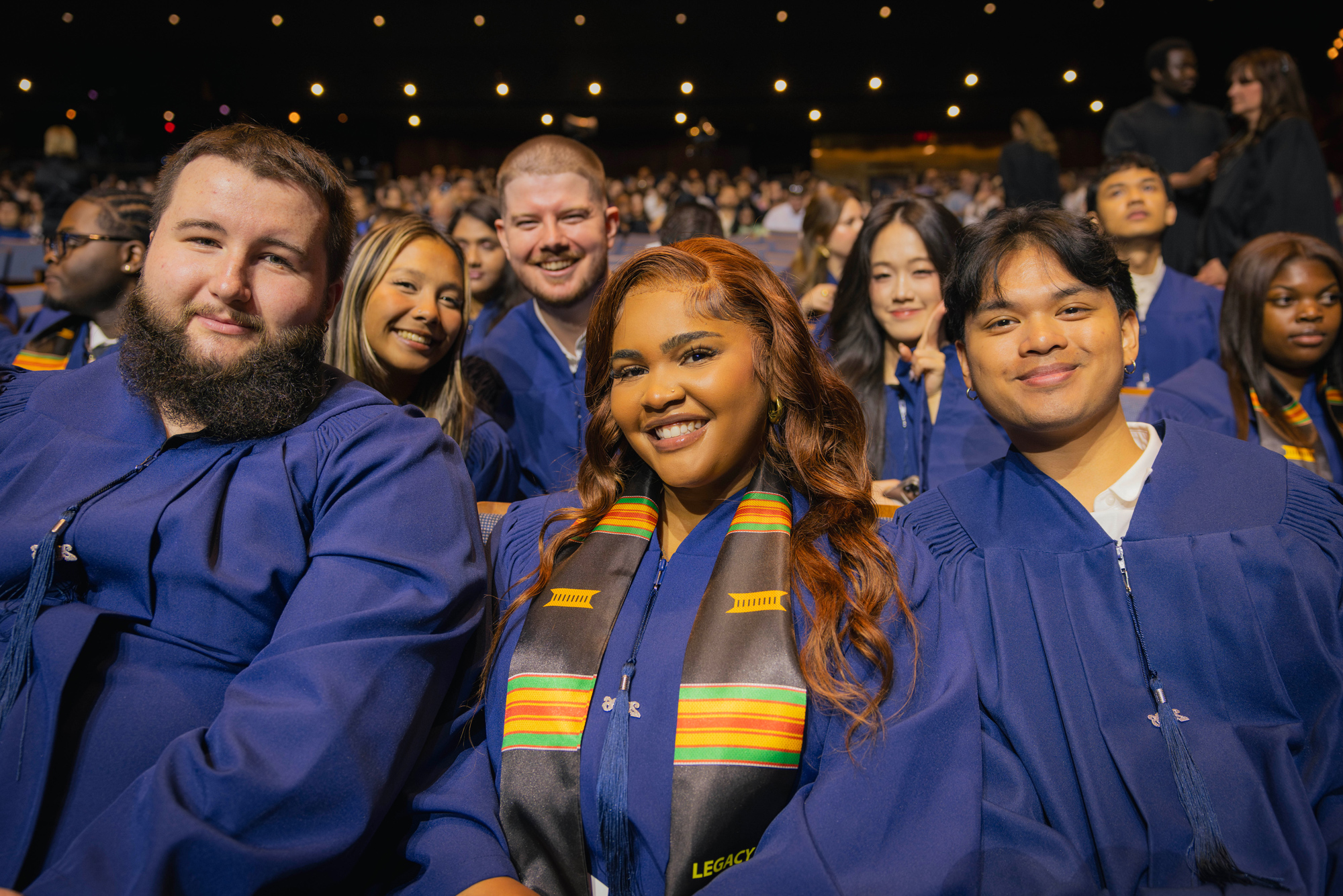 New grads seated in their robes at the 2026 convocation ceremonies smile for the camera.