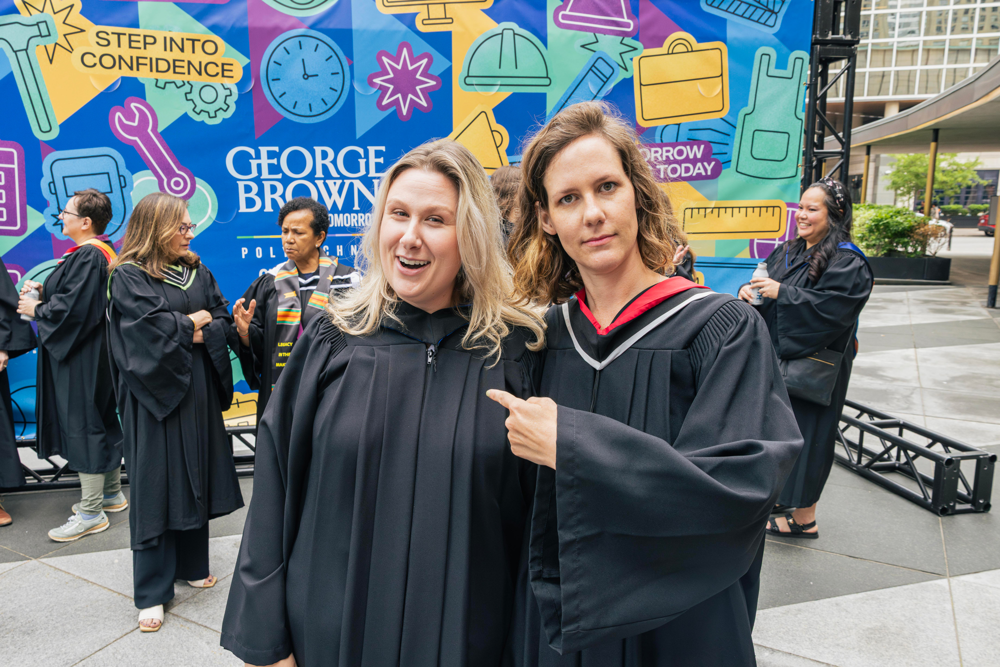 George Brown faculty in their gowns hug and smile at the convocation ceremony.