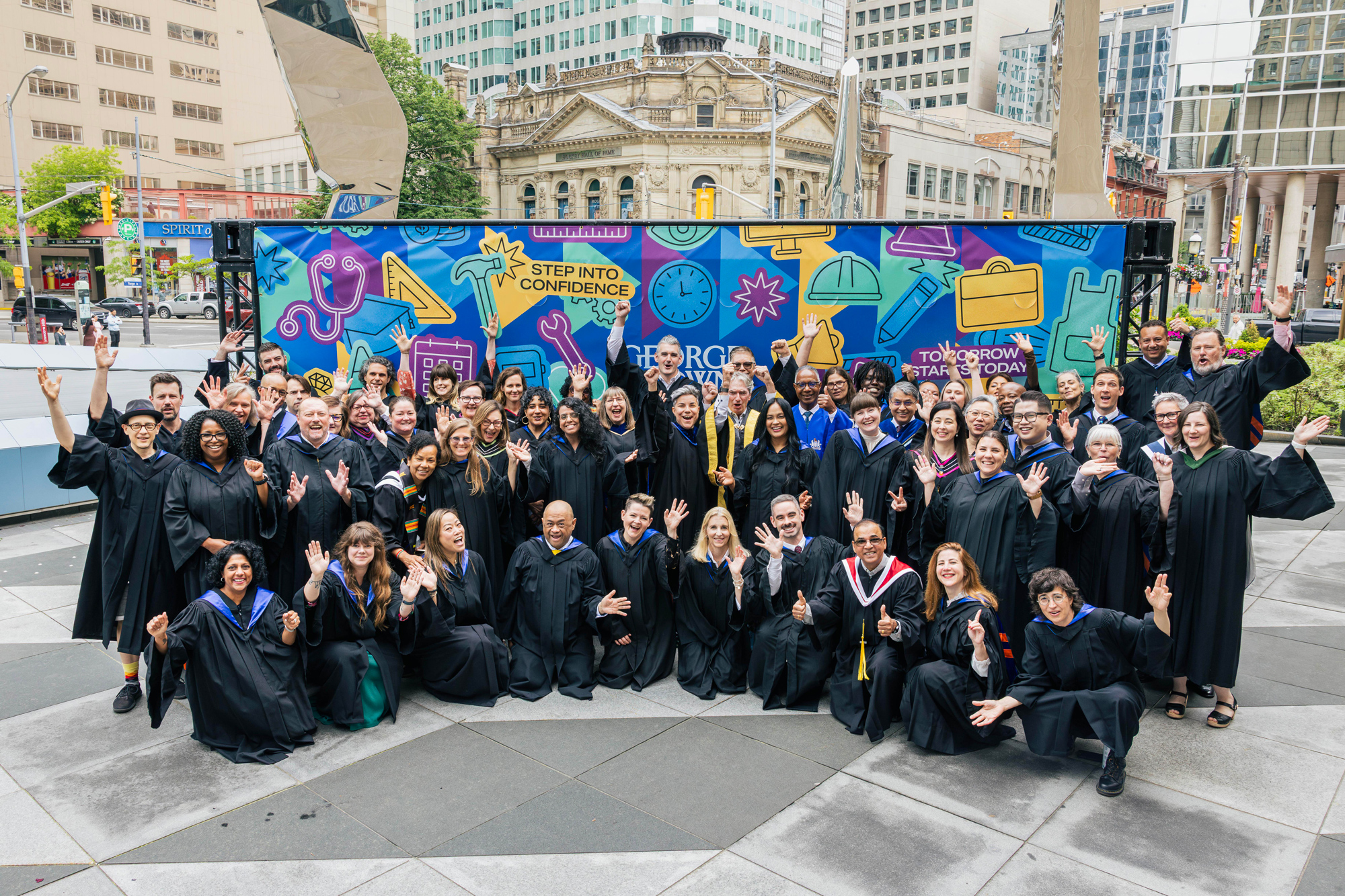 Faculty and staff pose for a group photo in front of the 2026 convocation mural.
