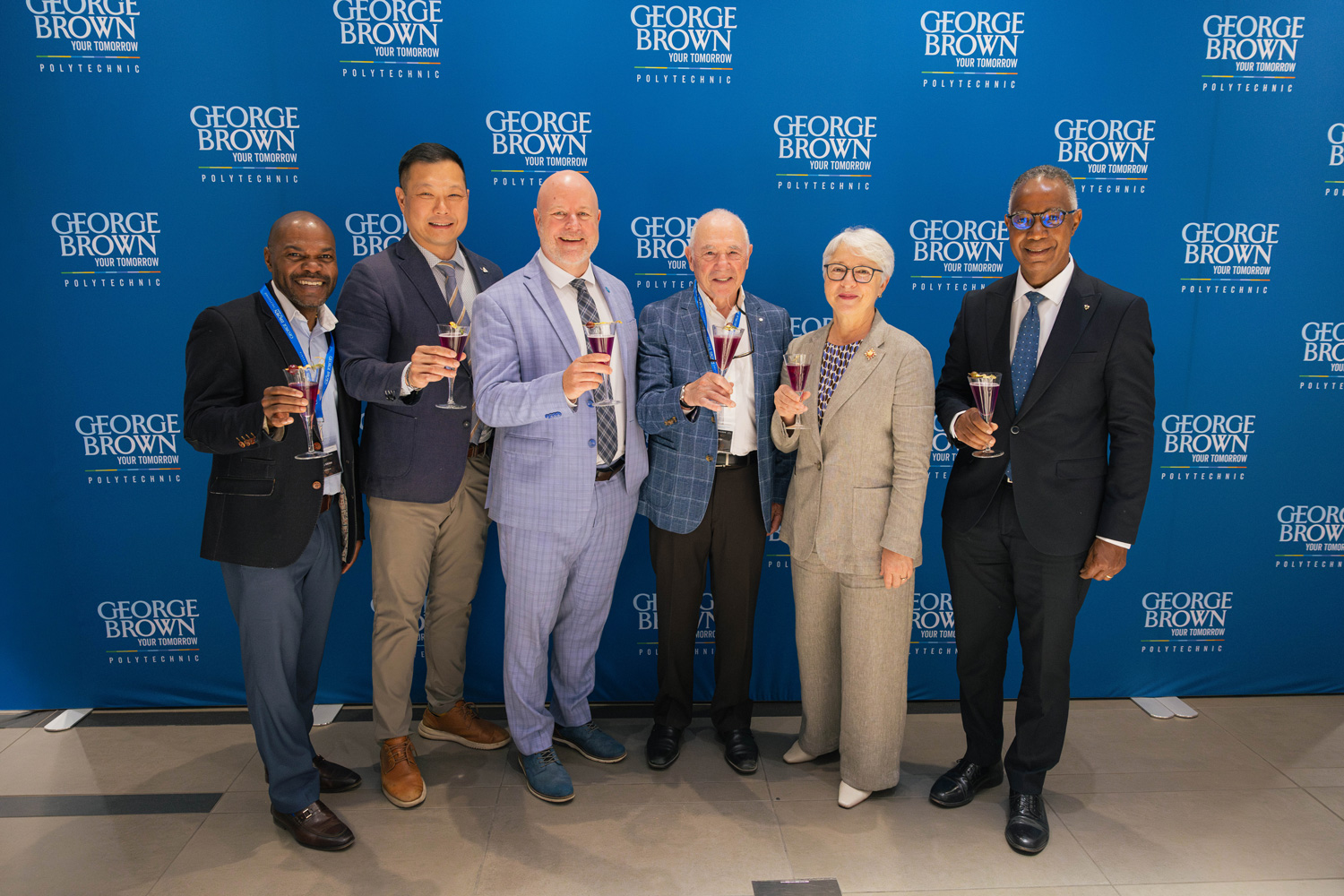 Ontario Wine Awards speakers pose together raising a glass against a blue George Brown backdrop.