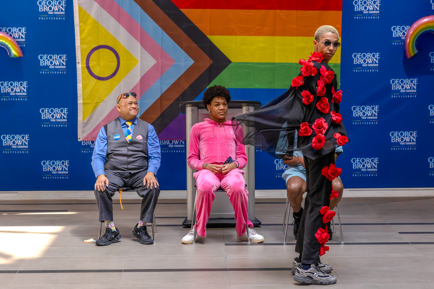 A ballroom performer in a black suit covered in roses poses in front of judges at the Pride kickoff event.
