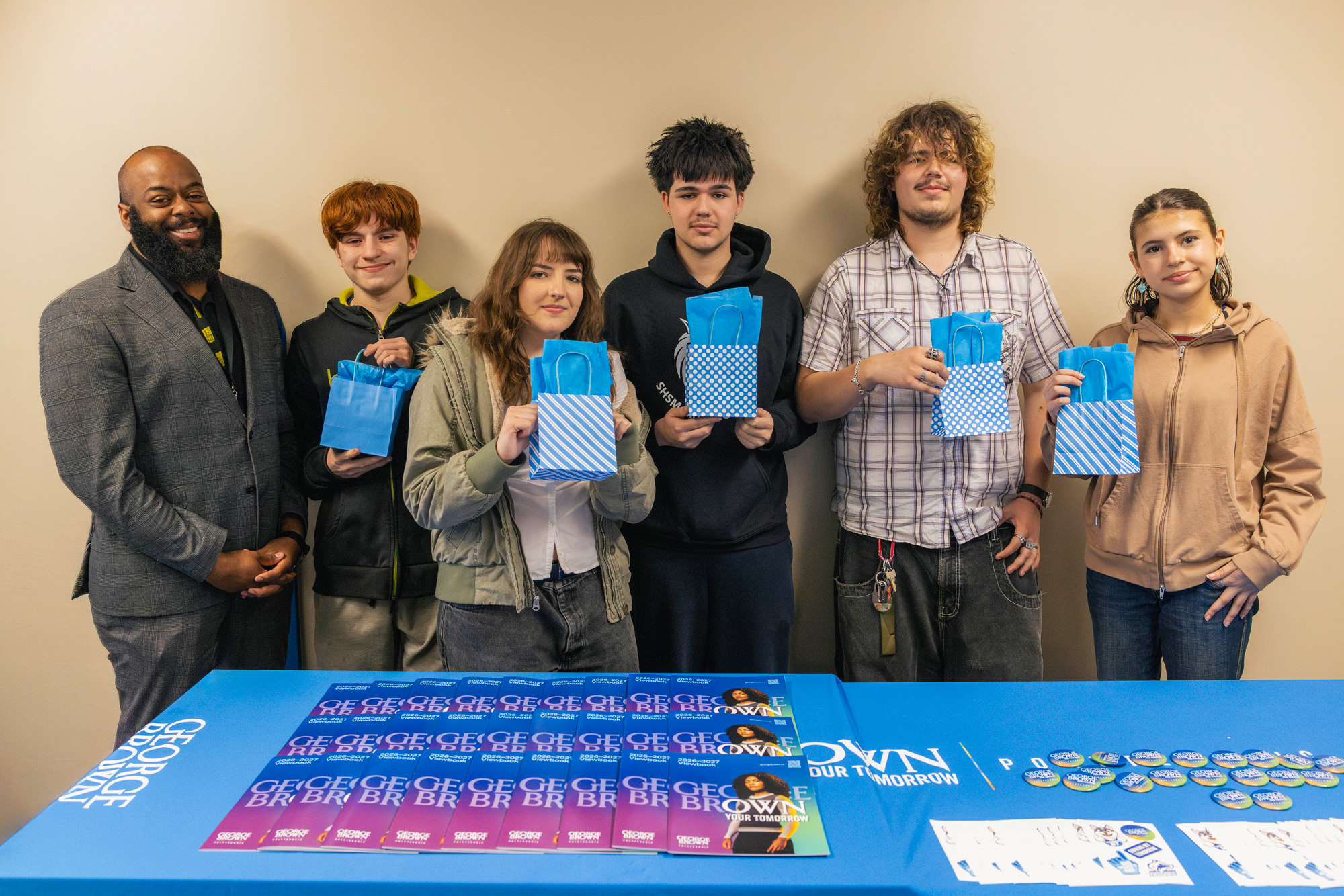 Visiting students at the Social Justice Conference from TDSB smile and pose with prize bags behind table with George Brown materials.