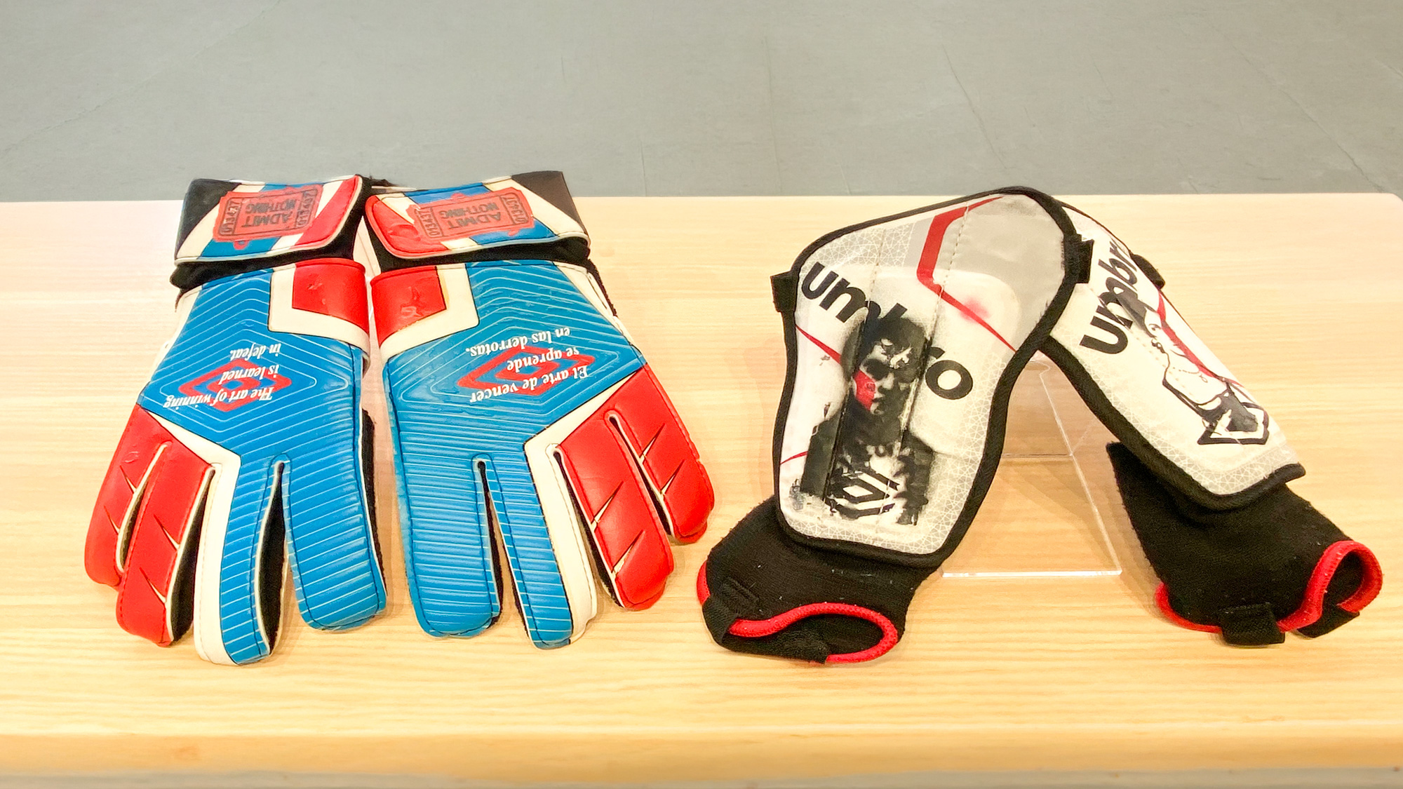 A pair of blue and red football gloves and shin guards imprinted with Venezualan and Trinidadian emblems.