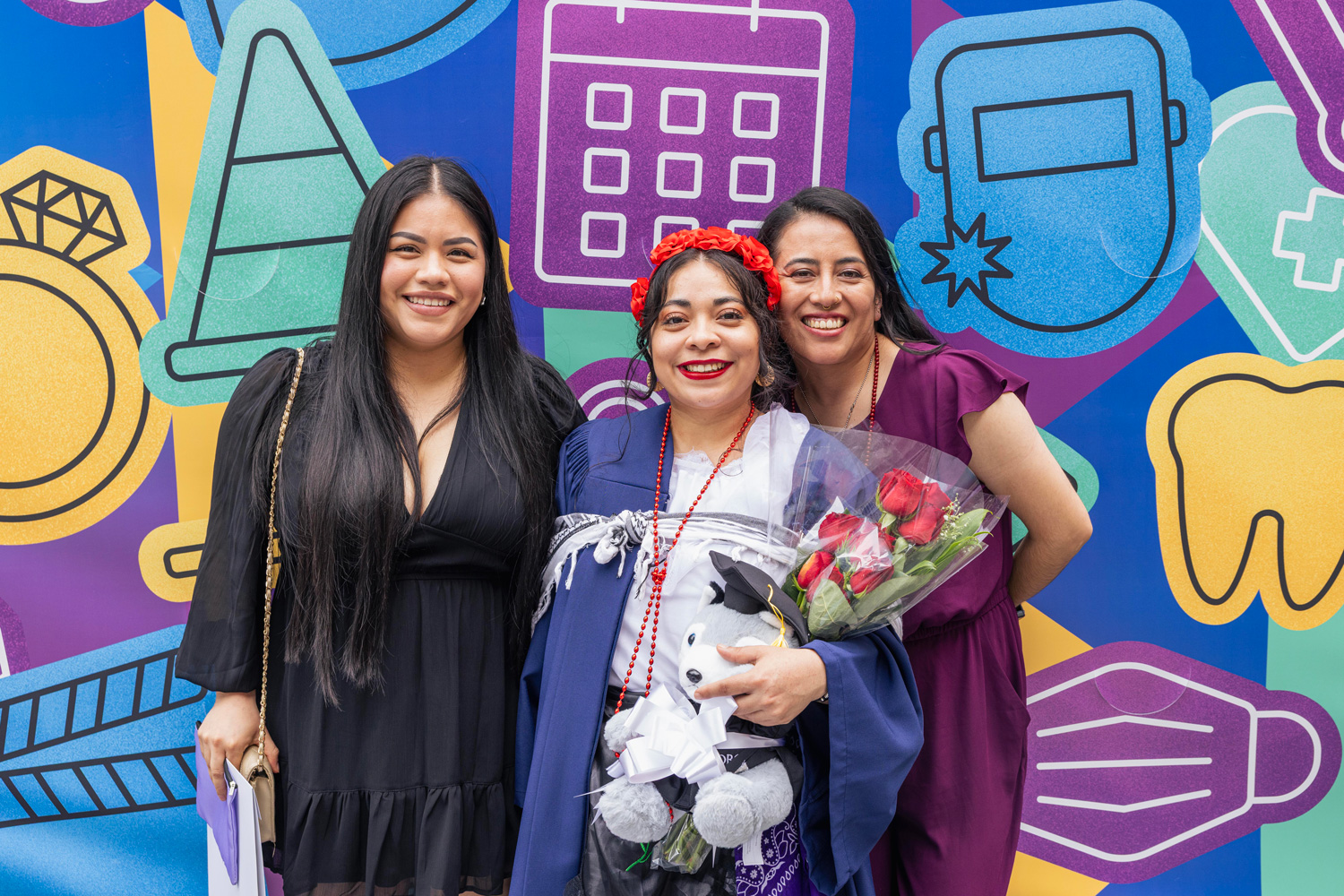 A new grad and their friends pose with a stuffed husky in front of a brightly coloured mural.