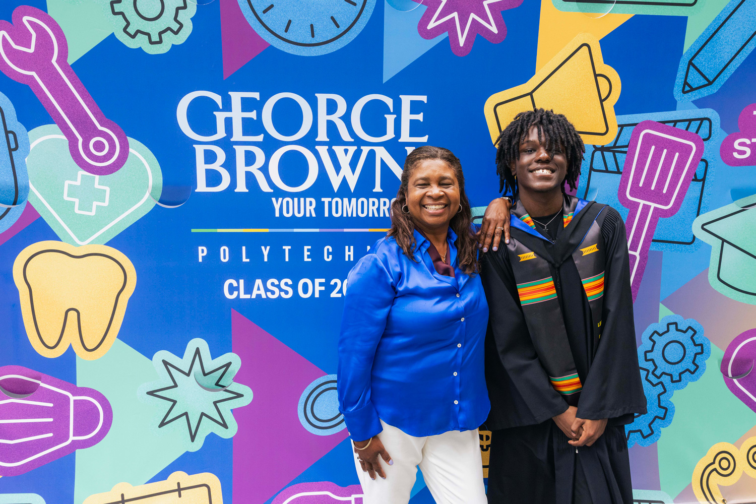 Staff pose with graduating students at convocation in front of the Class of 2026 mural.