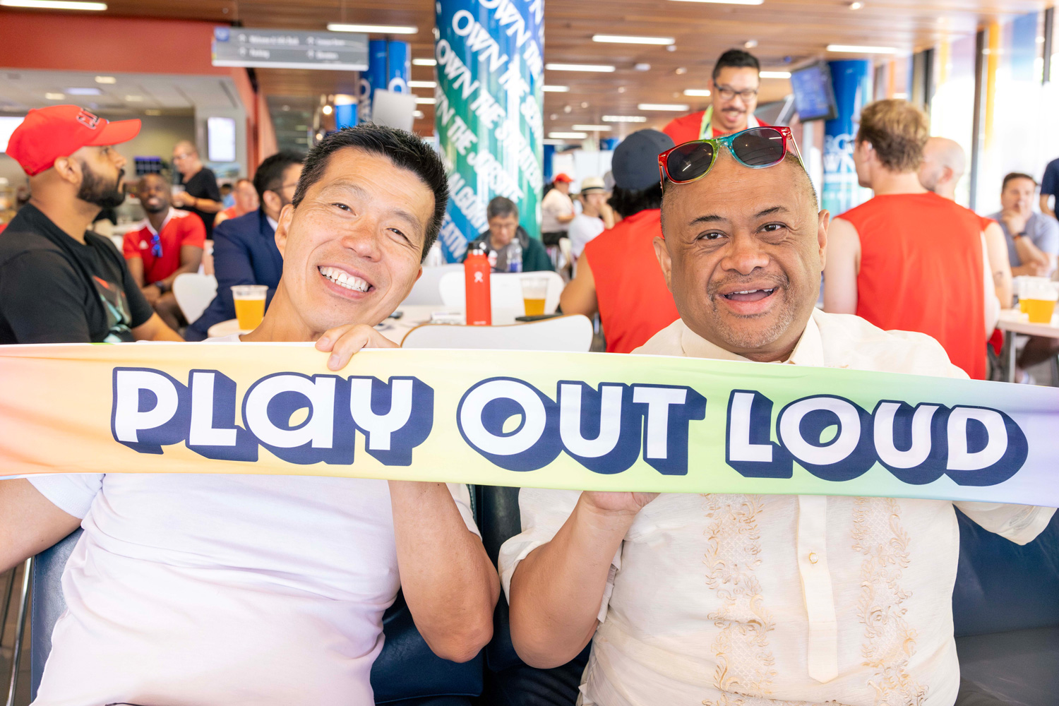 Guests at the FIFA Pride House hold a banner that says 'Play out loud'.
