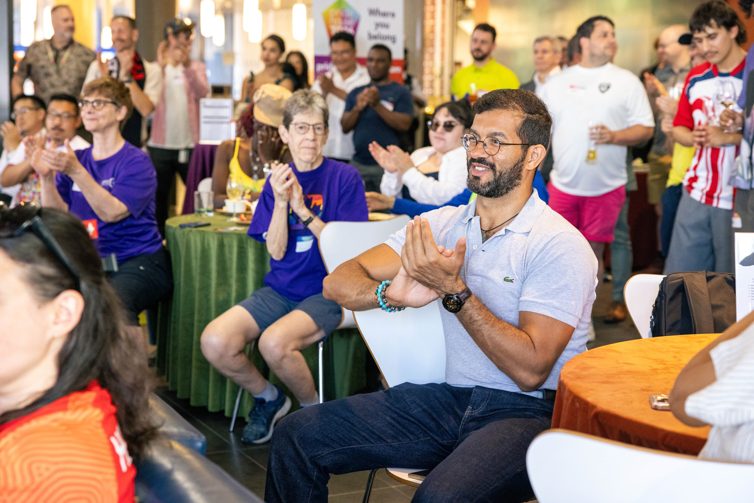 Guests clap and cheer watching Team Canada on the screens at the FIFA Pride House.